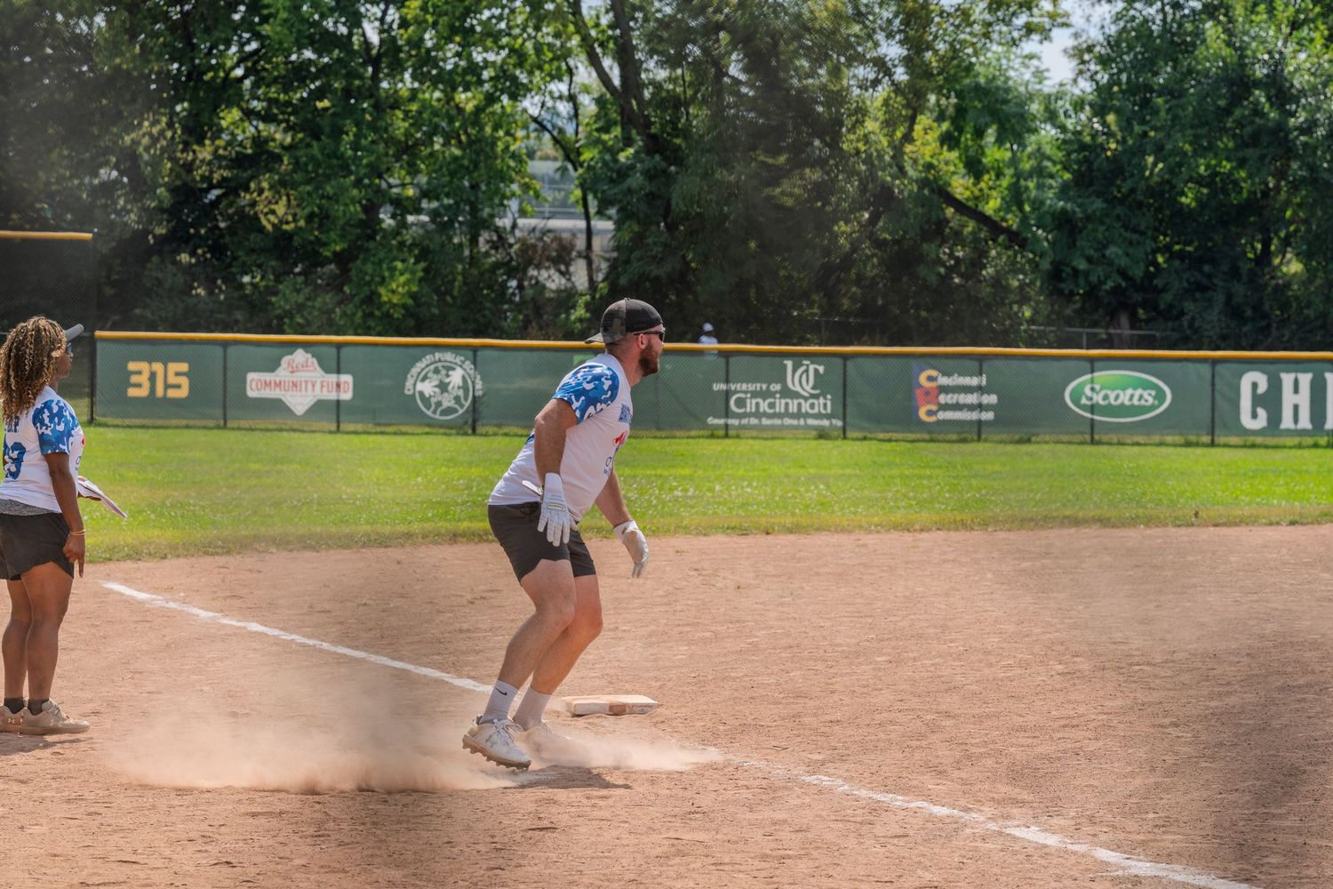 Male softball player running bases in a cloud of dust during an outdoor charity game.