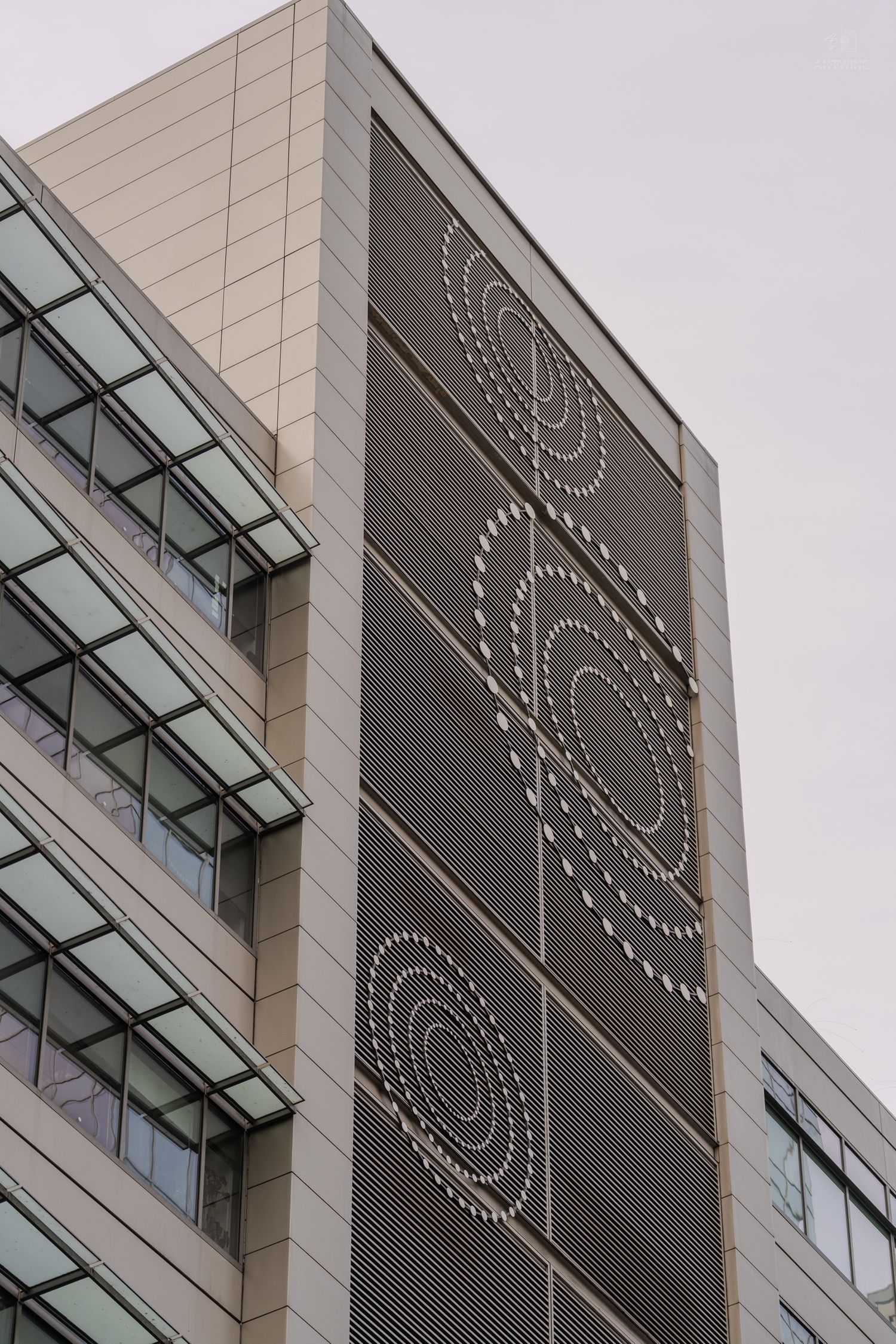 Modern office building facade with decorative circular dot pattern panels and glass windows against overcast sky.