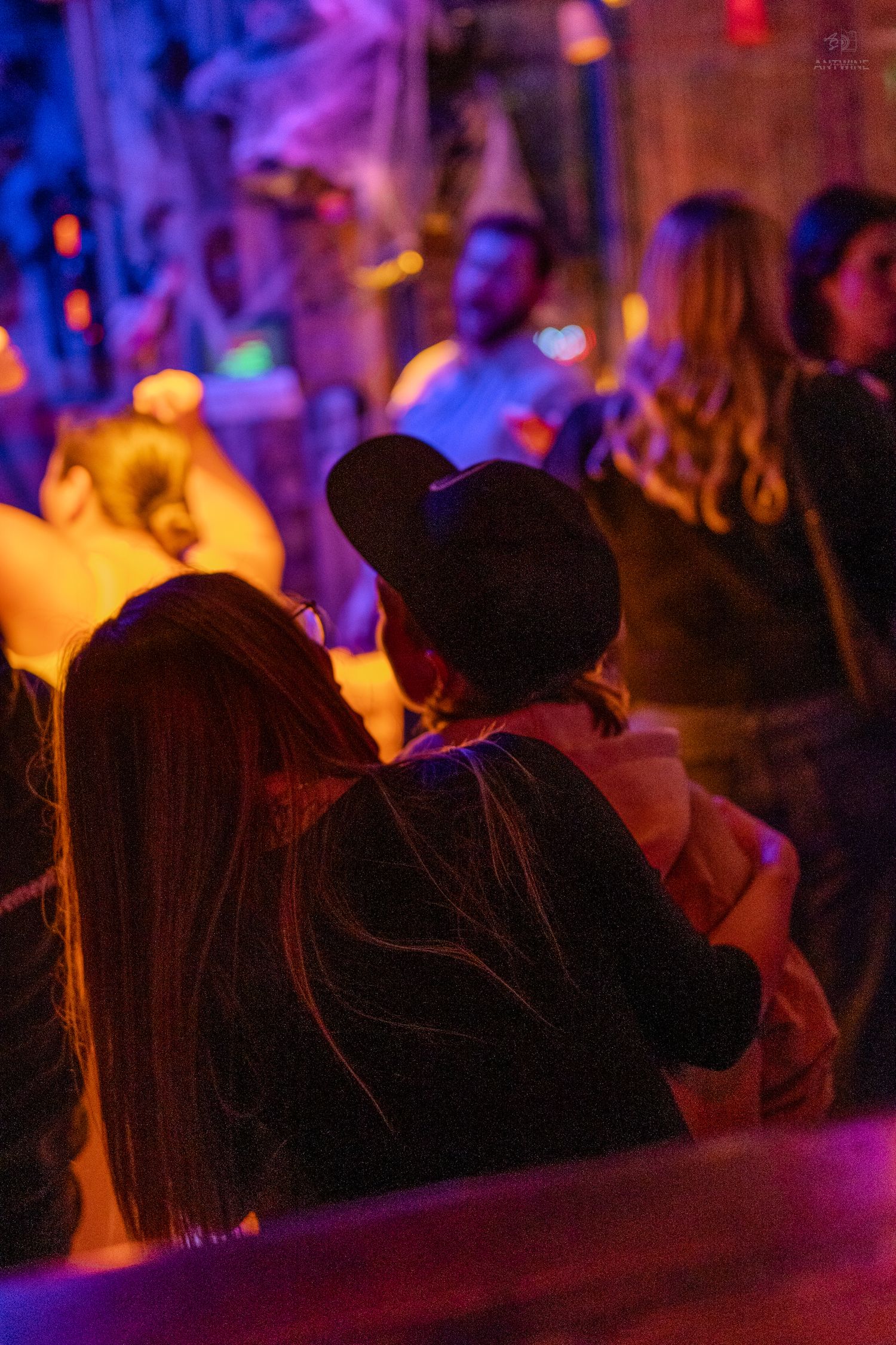 People enjoying a colorful nightclub event under vibrant purple and orange lighting.