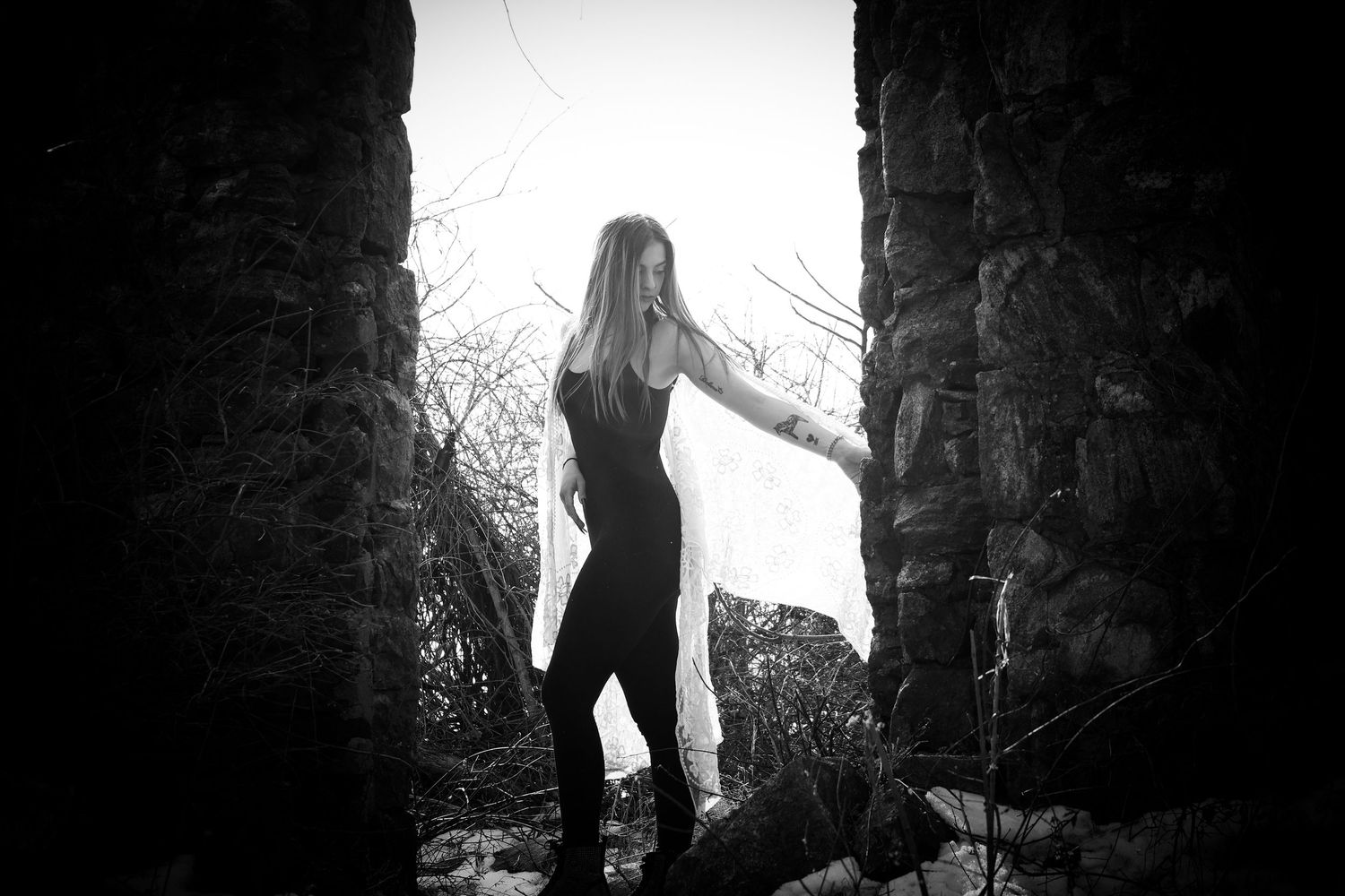 A black and white photo of a female standing in the middle of an old castle doorway.