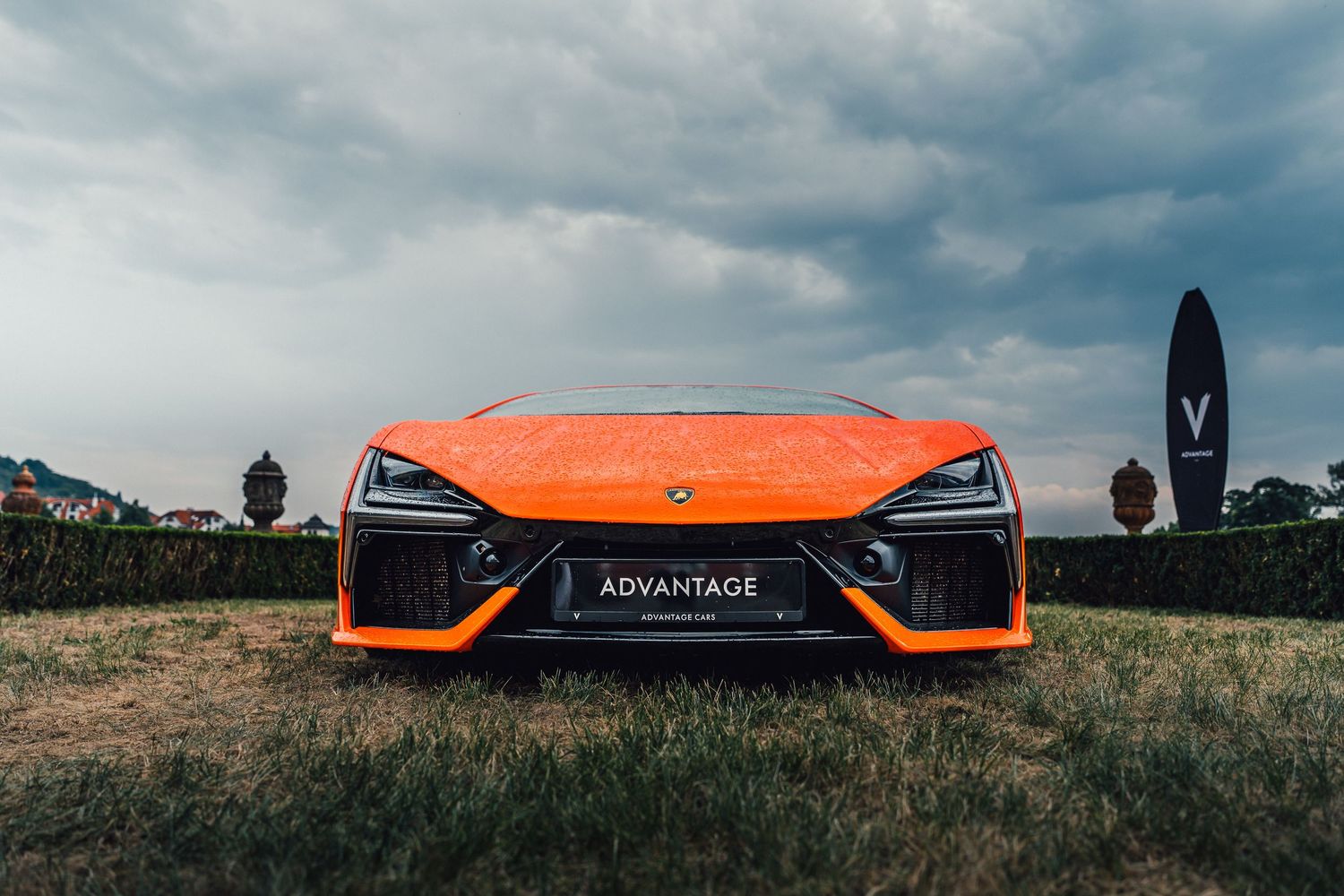 Orange Lamborghini supercar displayed front-facing at an outdoor automotive event under overcast skies.
