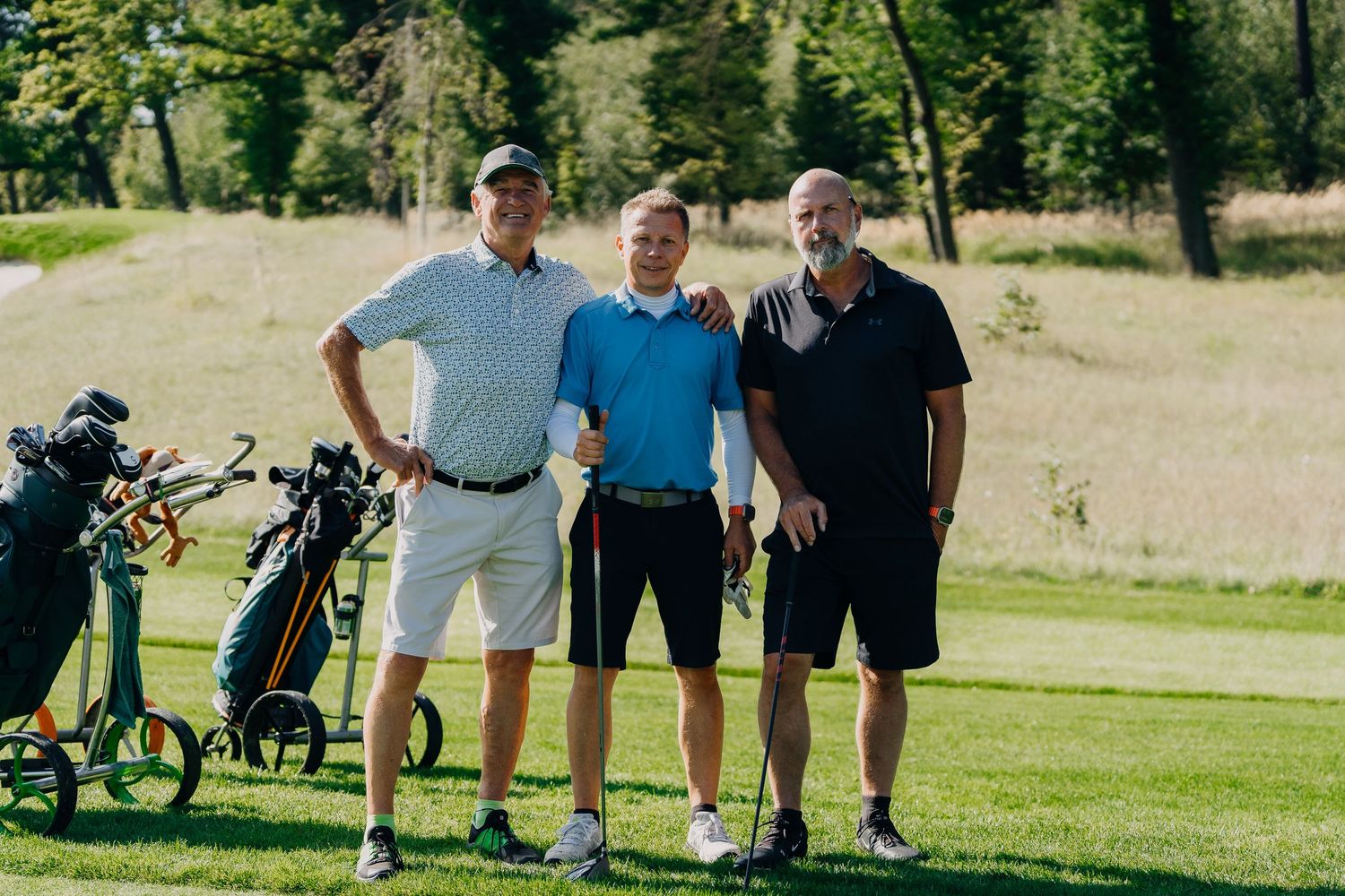 Three men posing together on a golf course with golf bags visible in the background.