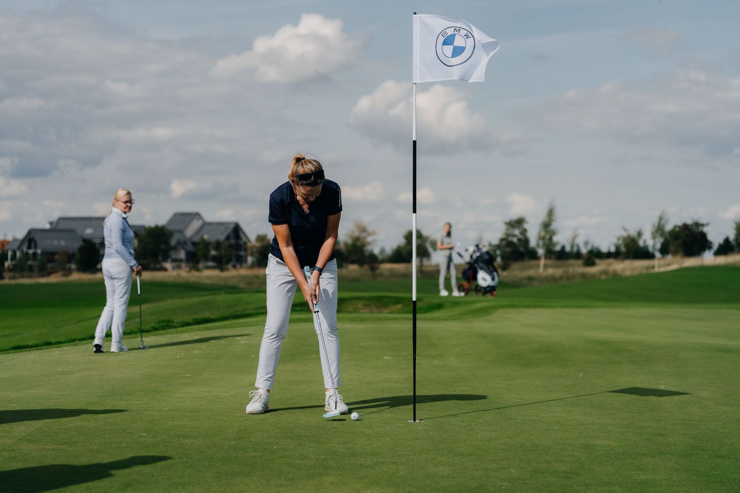 Golfer putting on a green near a BMW flag while another player stands in the background.