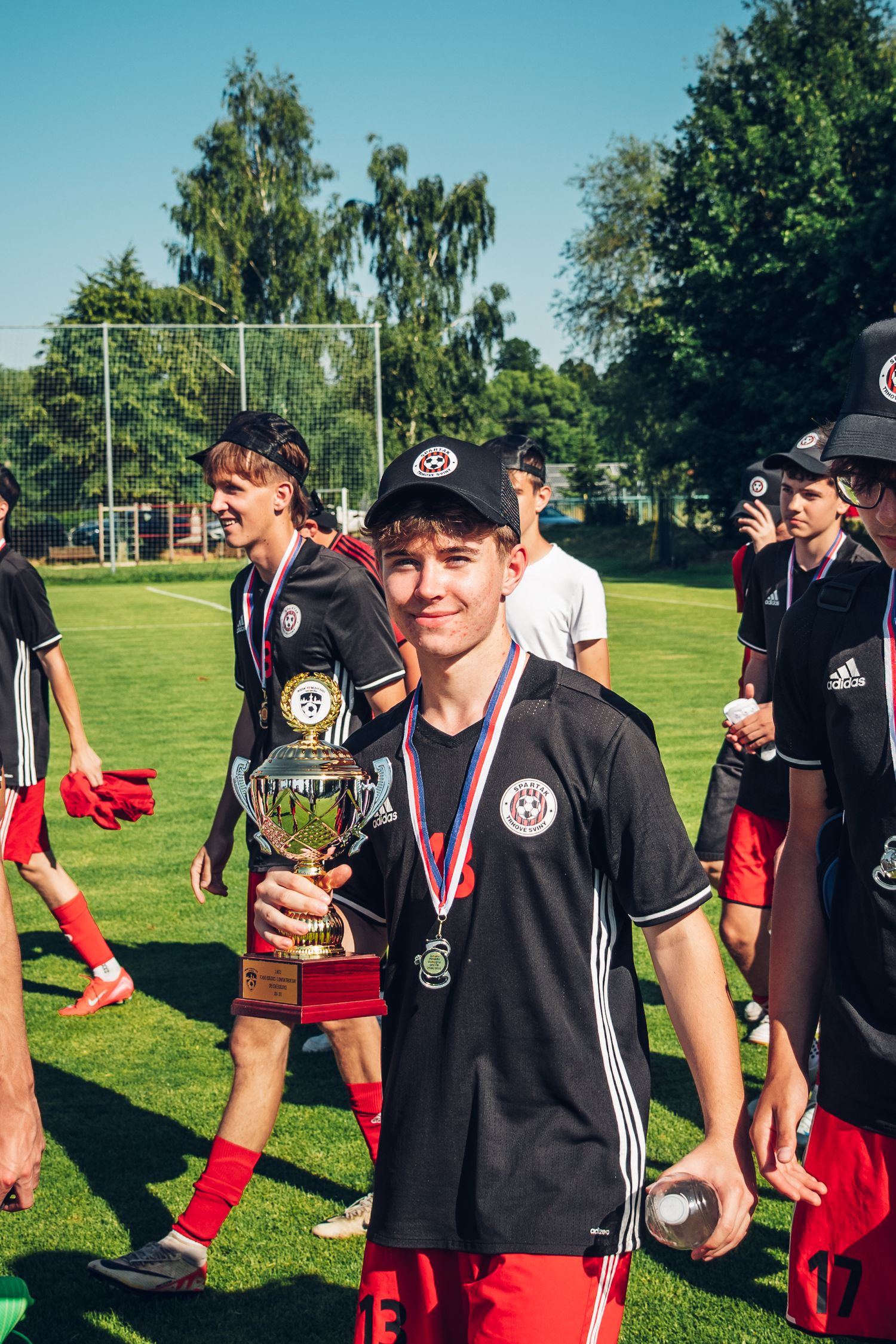 Smiling young soccer player holds trophy and medal after winning outdoor youth football tournament.