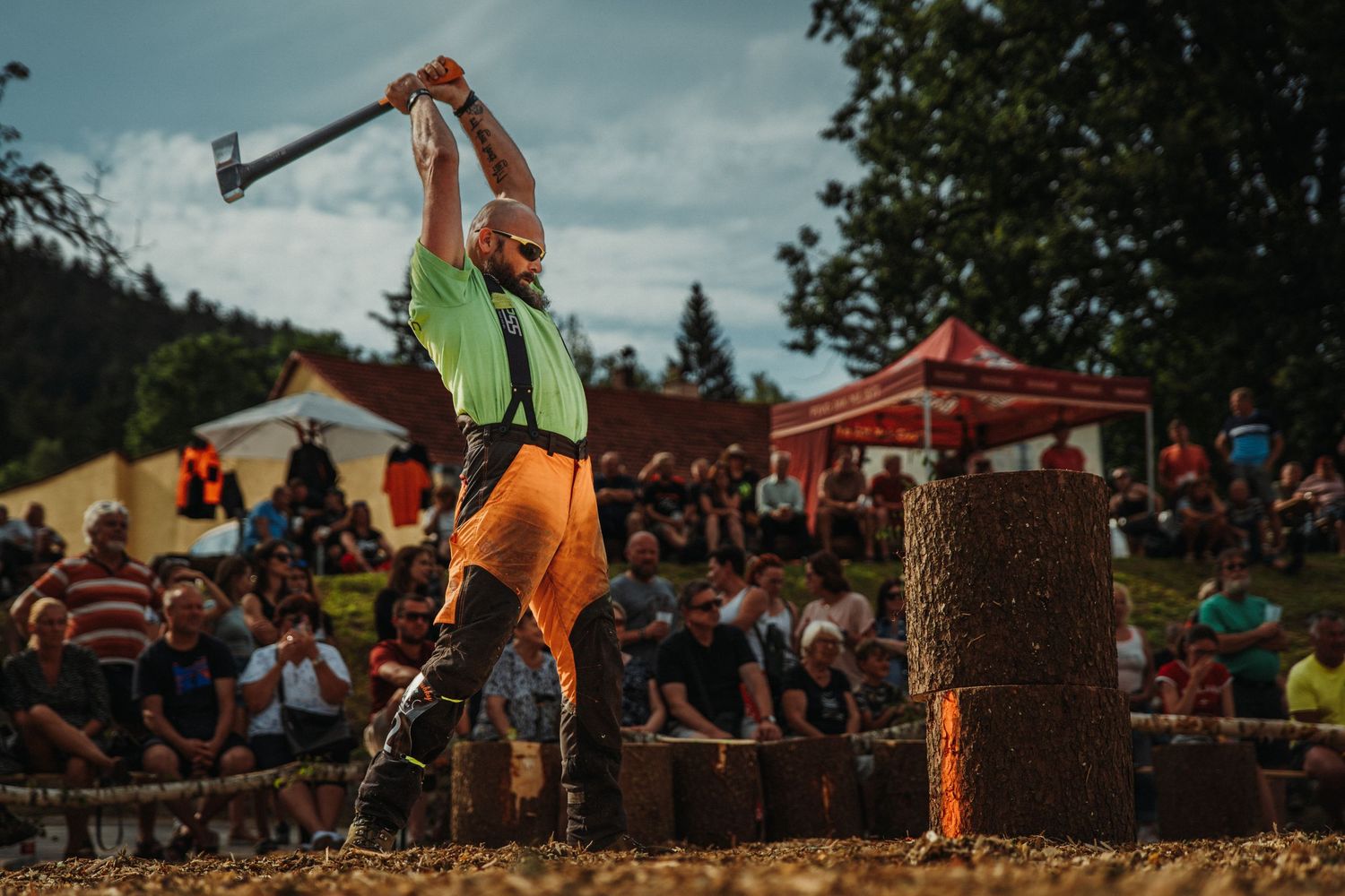 A lumberjack competitor swings an axe to split a log stump at an outdoor woodchopping competition before a crowd.