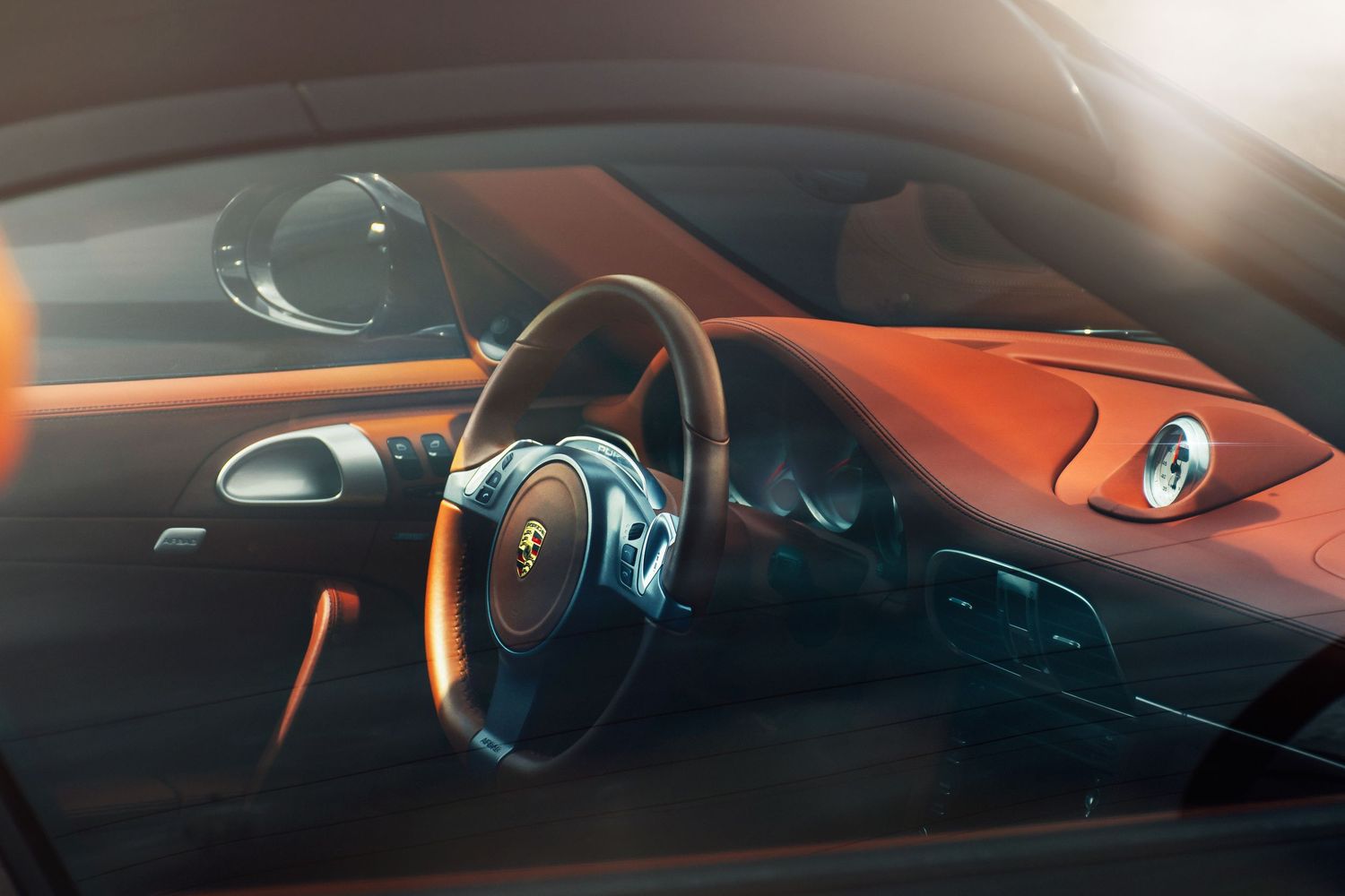 Interior view of a Porsche cockpit with steering wheel and orange dashboard bathed in sunlight.