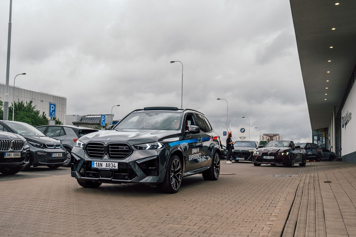 Dark BMW iX SUV parked outside a BMW dealership on an overcast day.