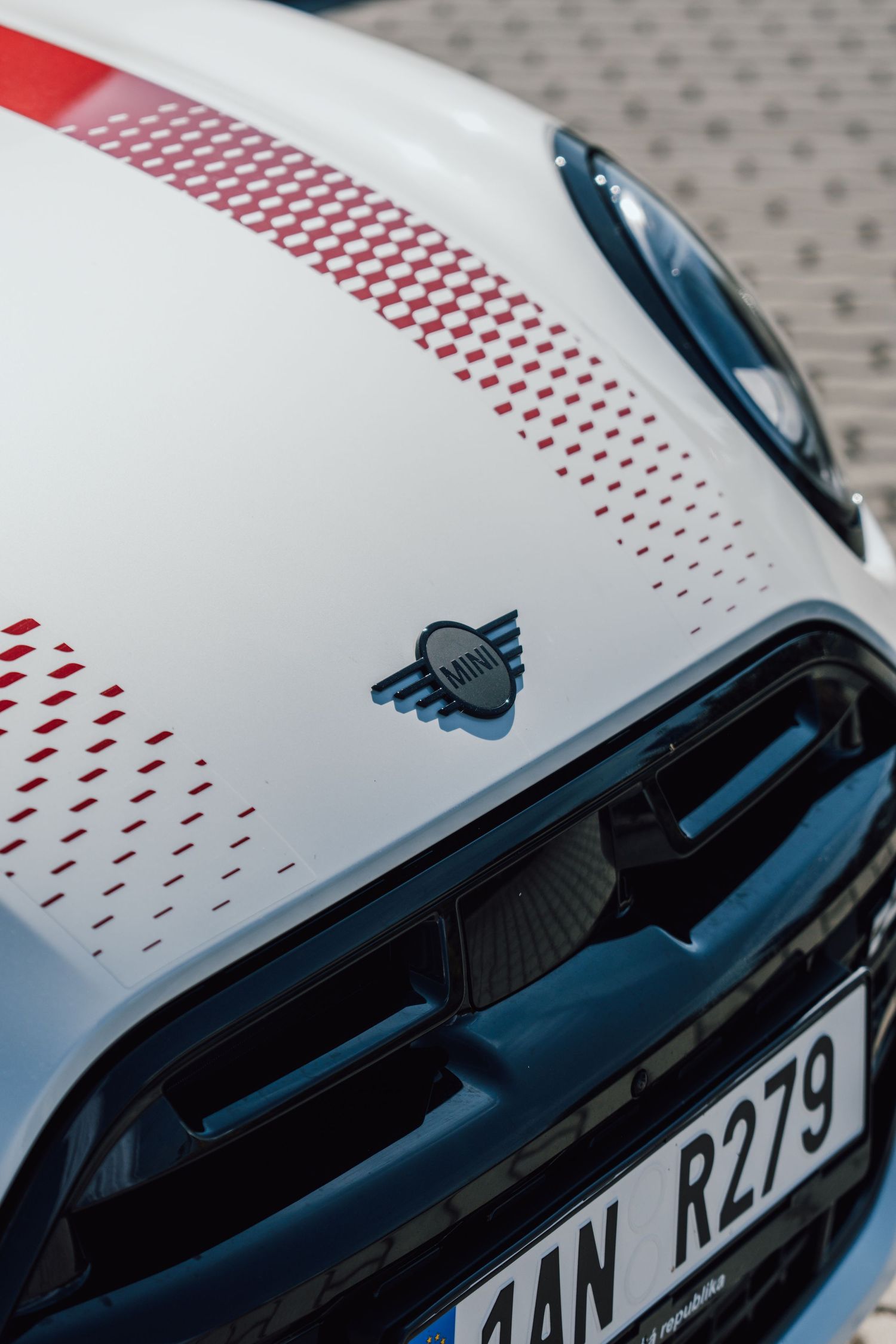 Close-up of MINI logo on white car hood with red geometric dot pattern graphic.