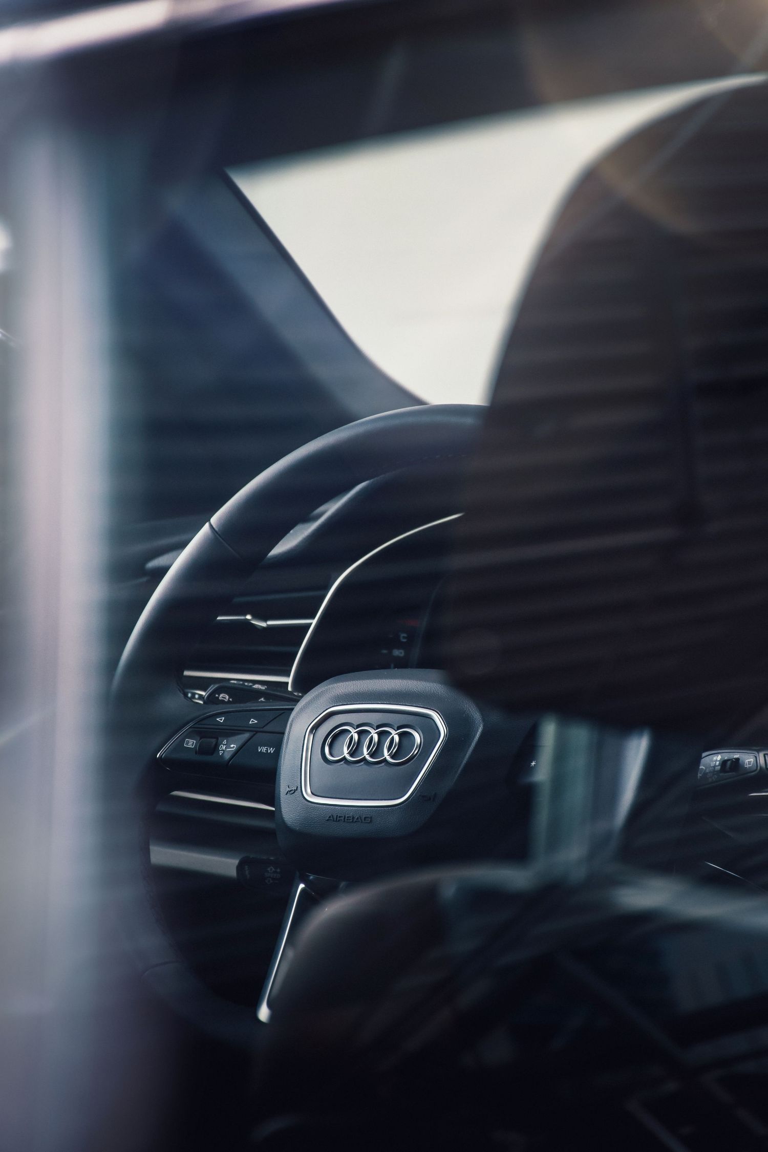 Close-up of an Audi steering wheel with iconic four-ring logo inside a luxury vehicle interior.