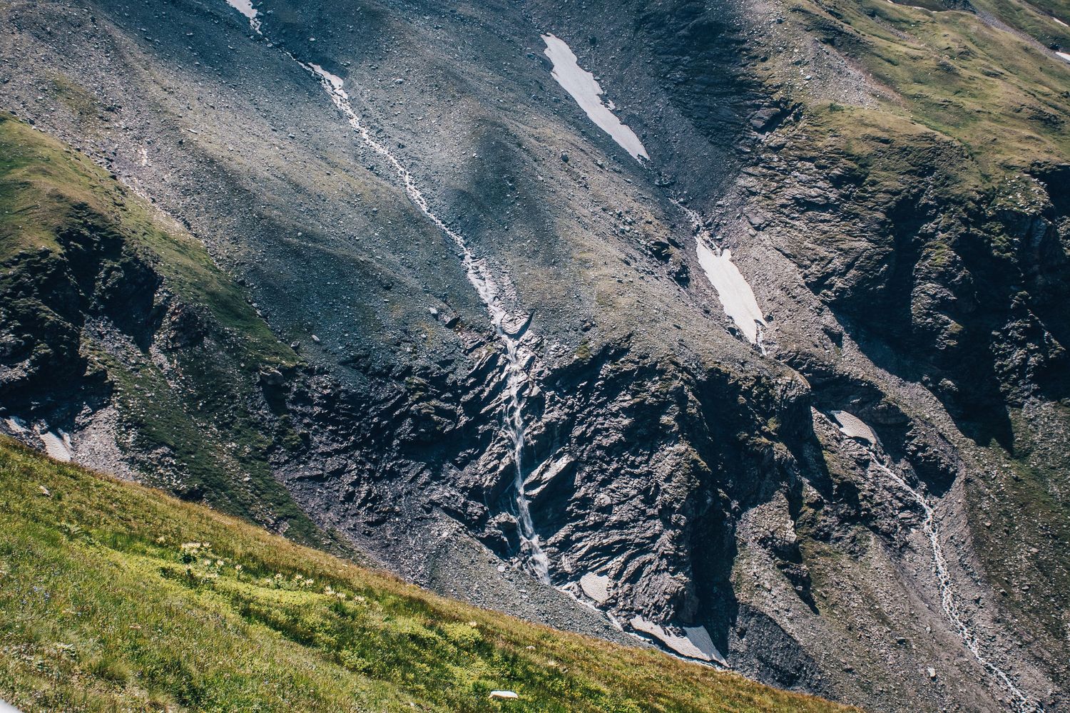 Rocky mountain cliff face with thin waterfalls and patches of snow on steep terrain.