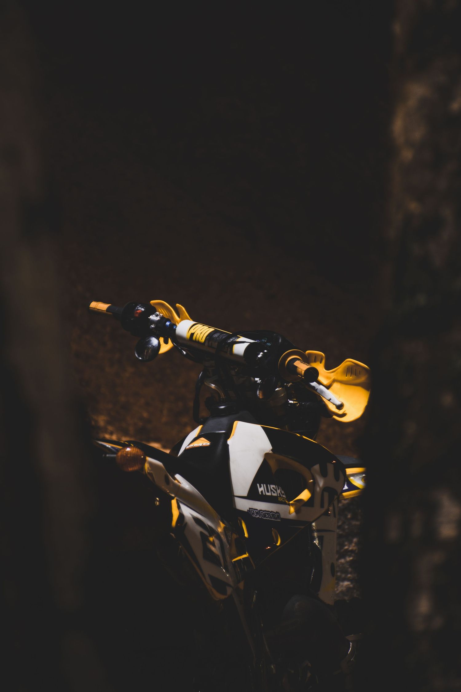 Close-up of a Husqvarna dirt bike handlebar with gold grips in a dark setting.