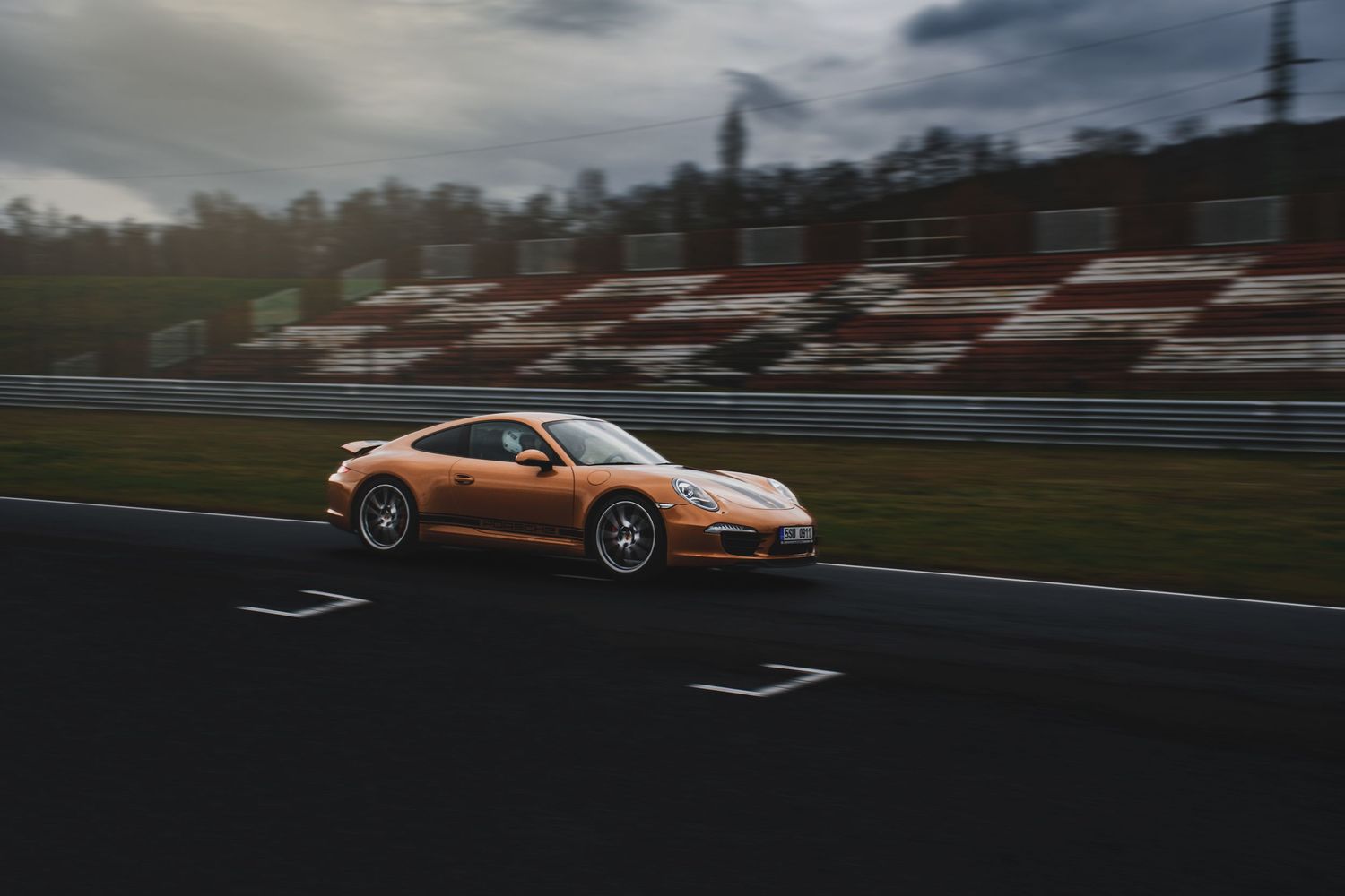 Orange Porsche 911 Turbo speeding along a race track with motion blur background.