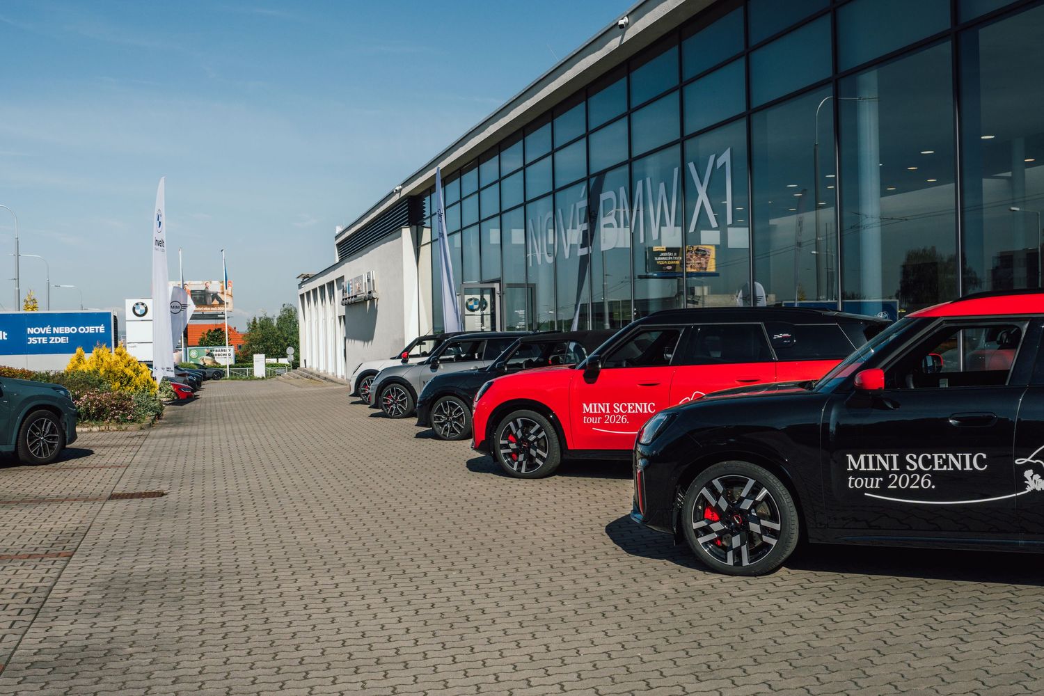 Row of red and black MINI Scenic tour 2026 cars parked outside BMW dealership.