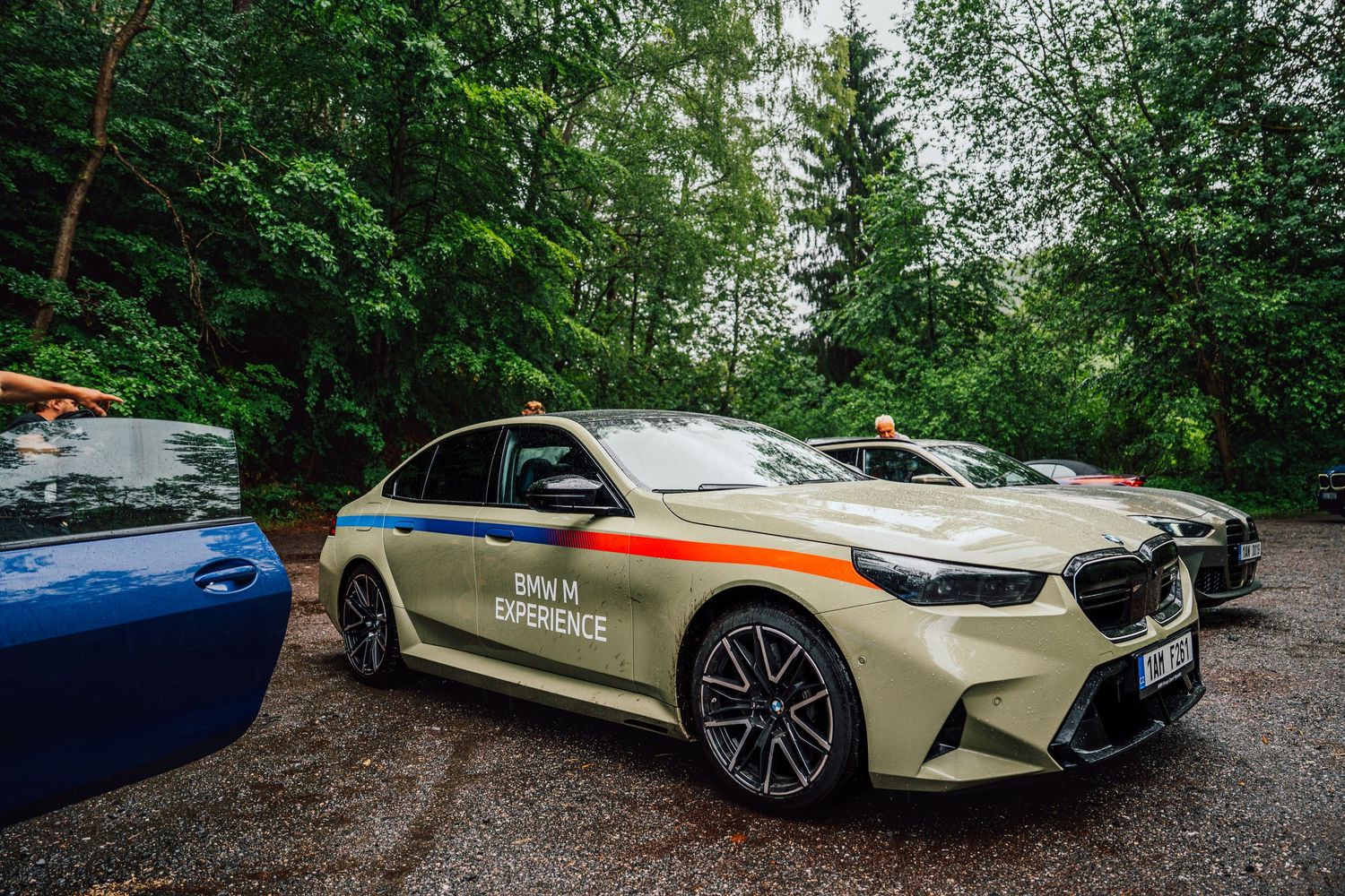BMW M Experience special edition sedan in beige livery parked near dense green forest.