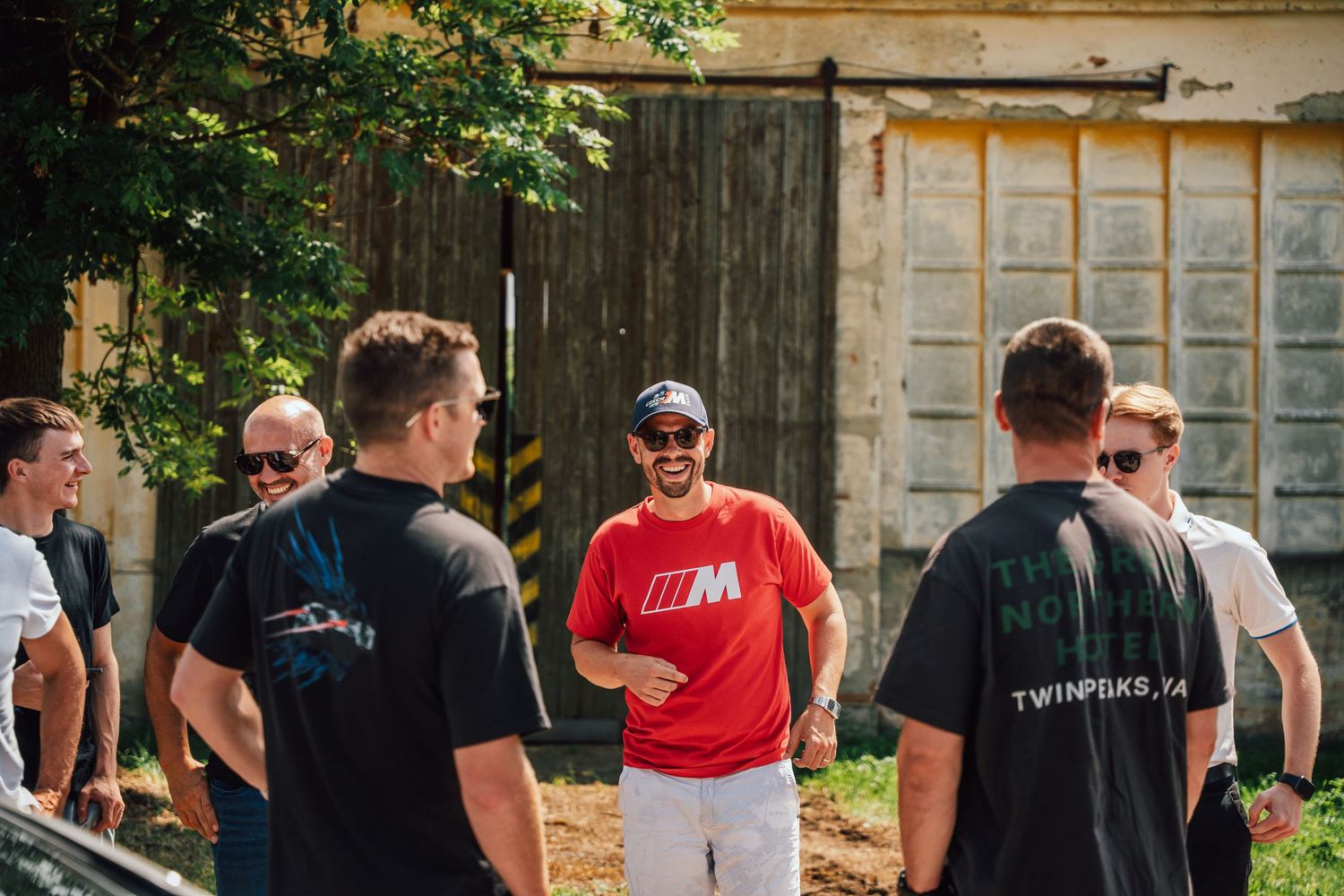 Group of BMW enthusiasts in M-branded apparel socializing outdoors at a car meet event.