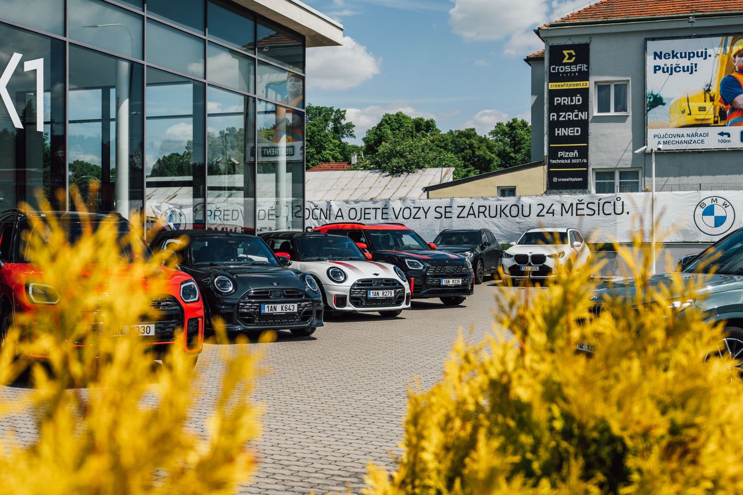 Several MINI Cooper cars displayed in a BMW dealership forecourt on a bright sunny day.