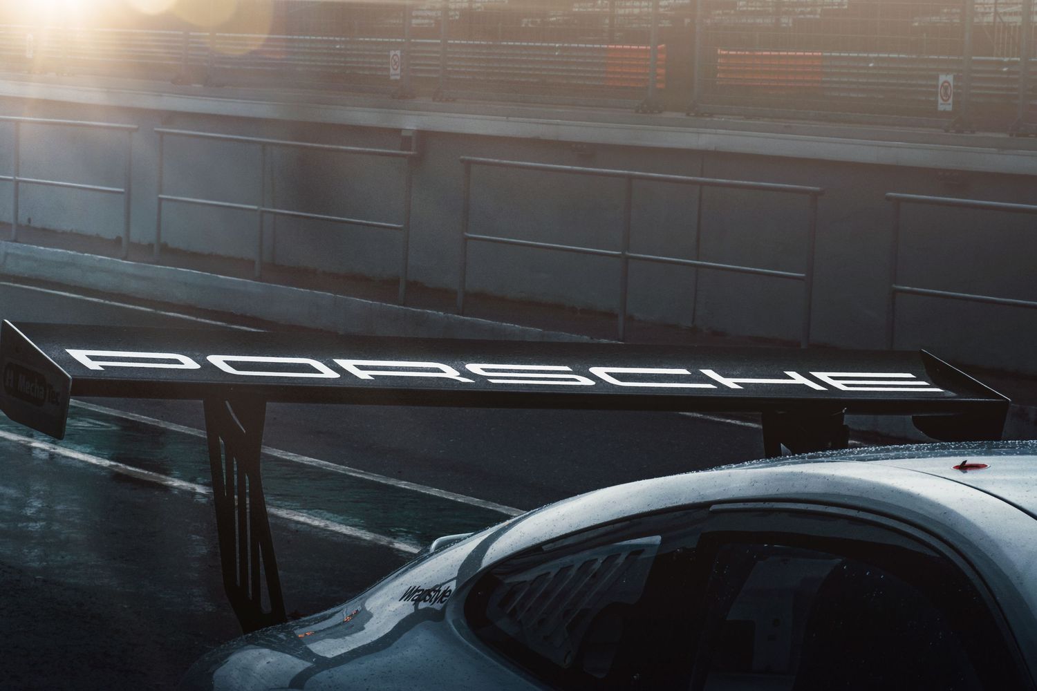 Close-up of a Porsche rear wing with illuminated Porsche lettering on a race car.