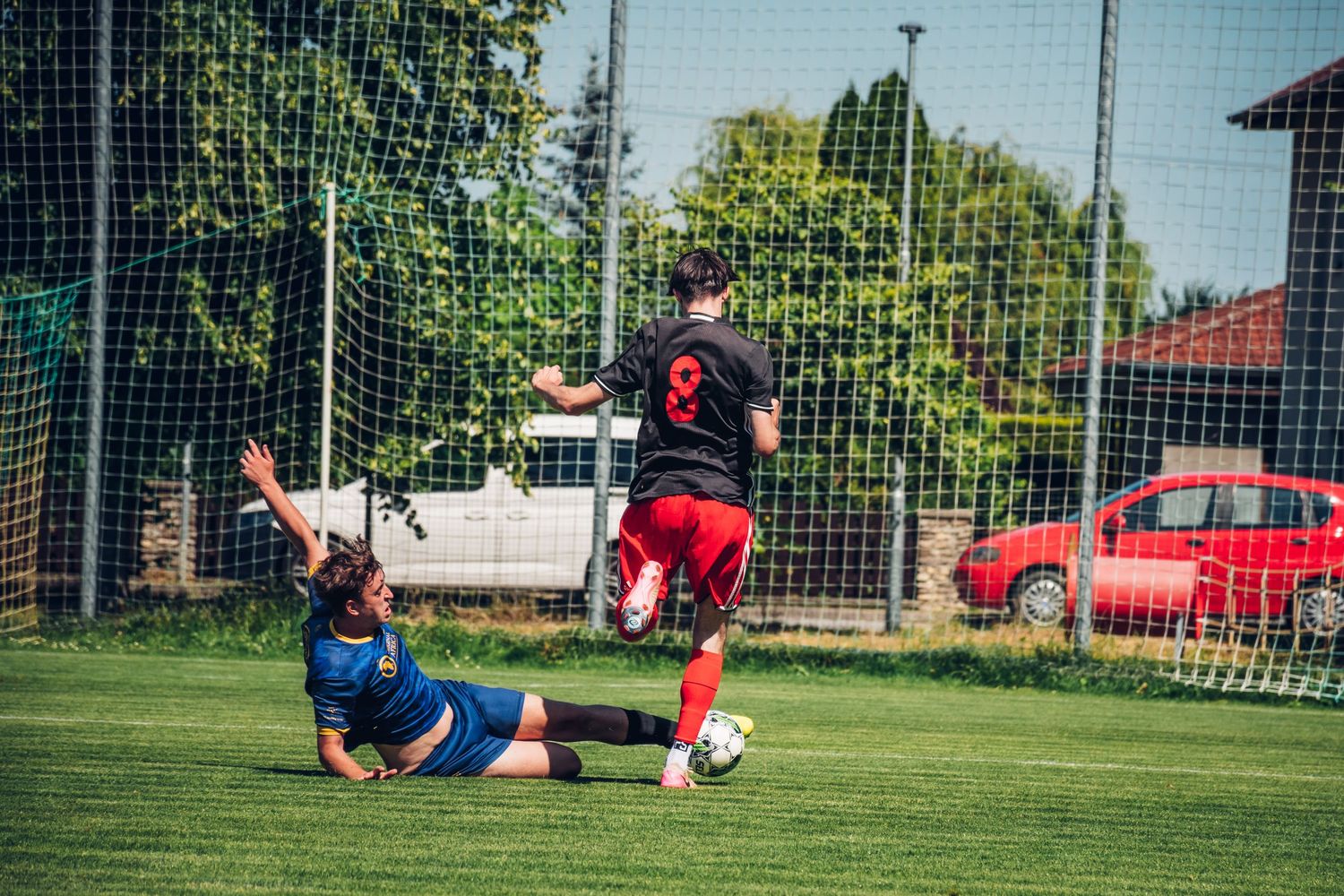 Soccer player in red slides to tackle opponent during an intense outdoor youth football match.