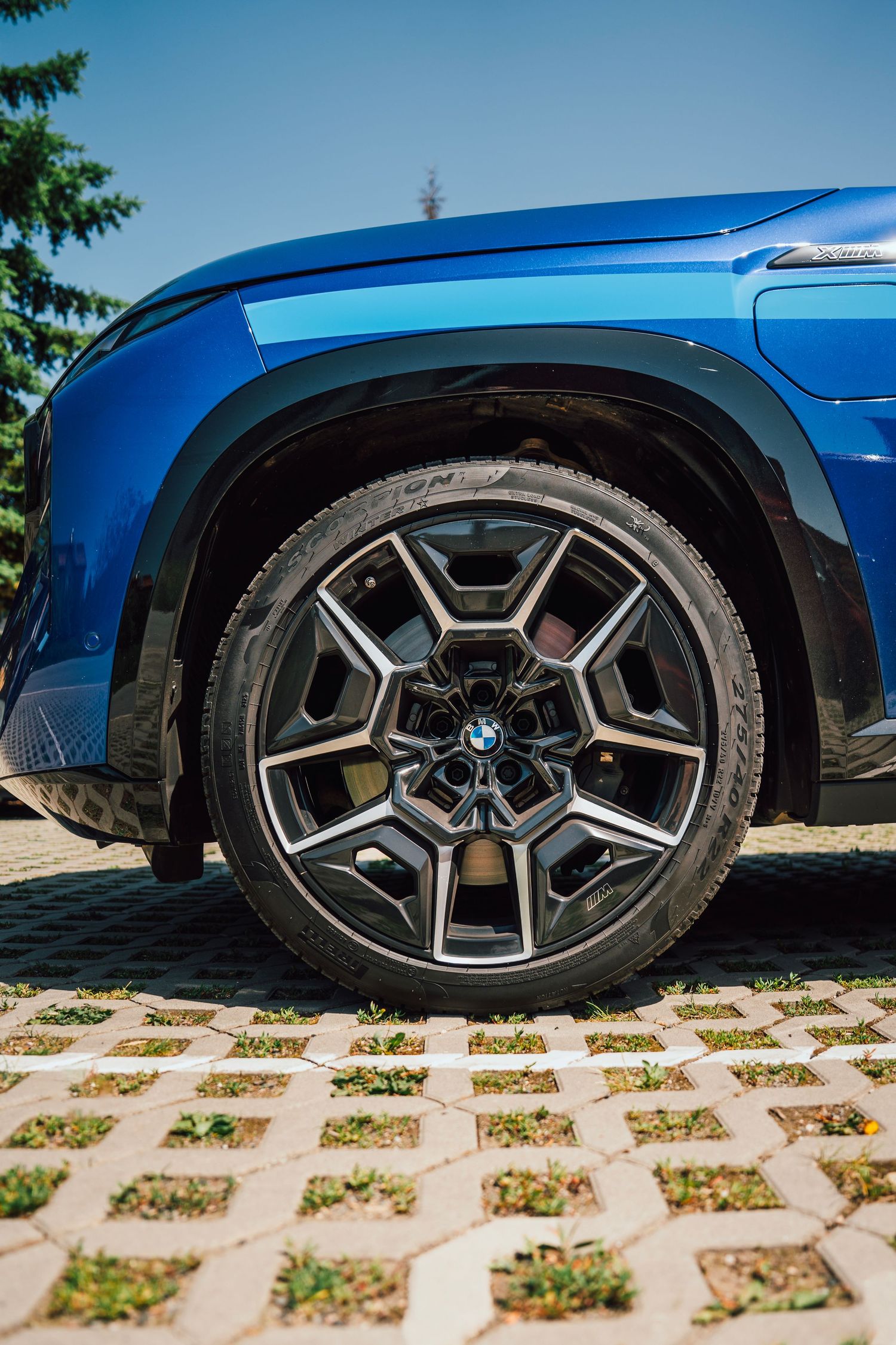 Close-up of a blue BMW SUV front wheel featuring a distinctive multi-spoke alloy rim on a paved surface.