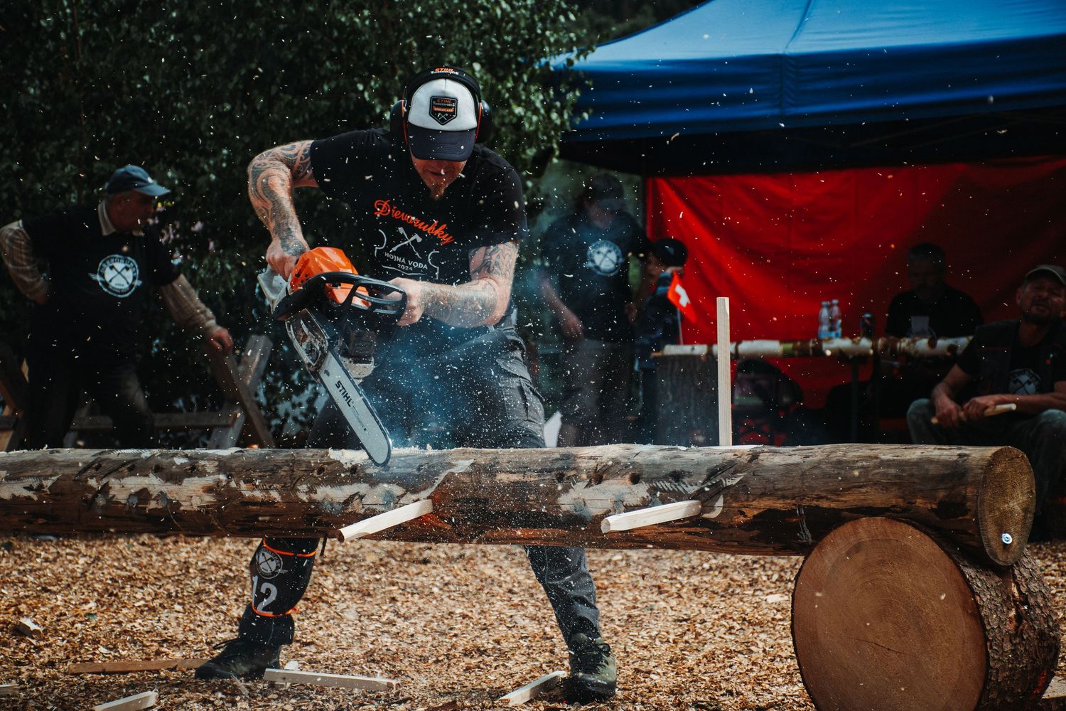 Competitor uses chainsaw to cut through large log during outdoor lumberjack competition with sawdust flying.