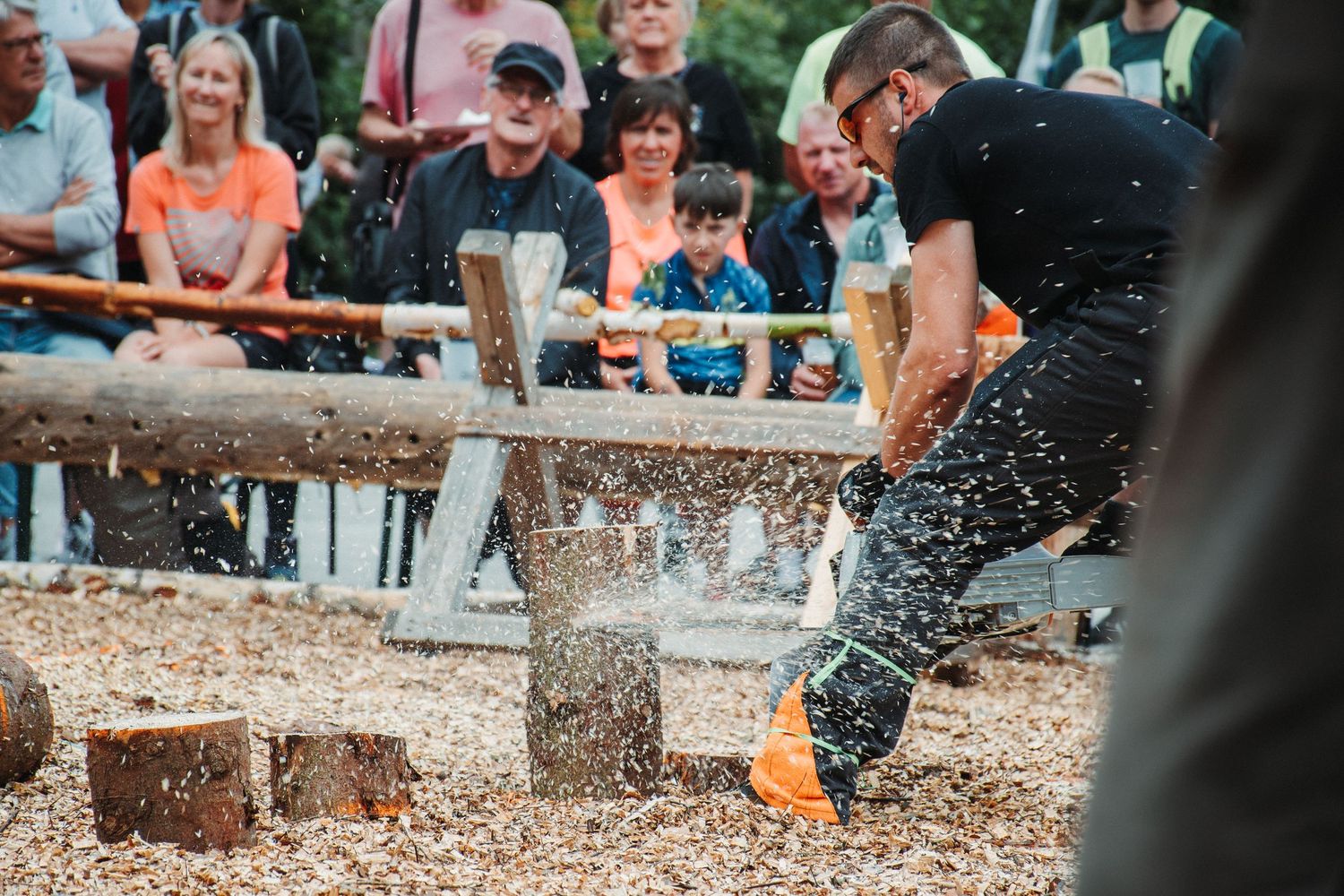 Lumberjack competitor swings axe through wood log as crowd watches at outdoor chopping competition.