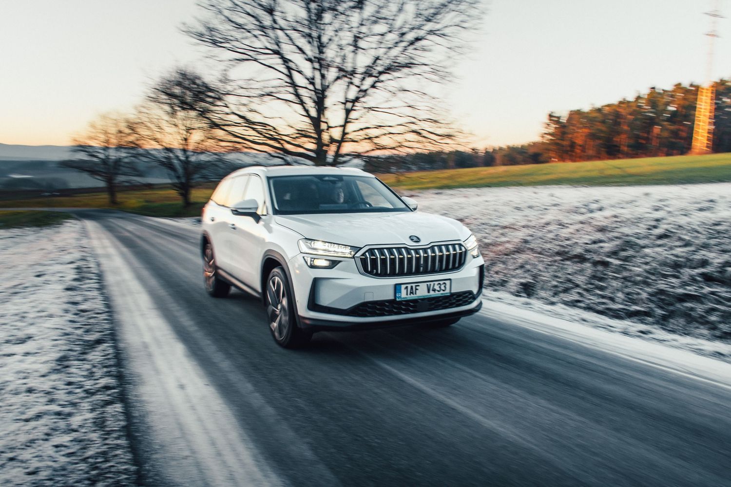 White Skoda SUV driving on a lightly snow-dusted road in winter morning light.