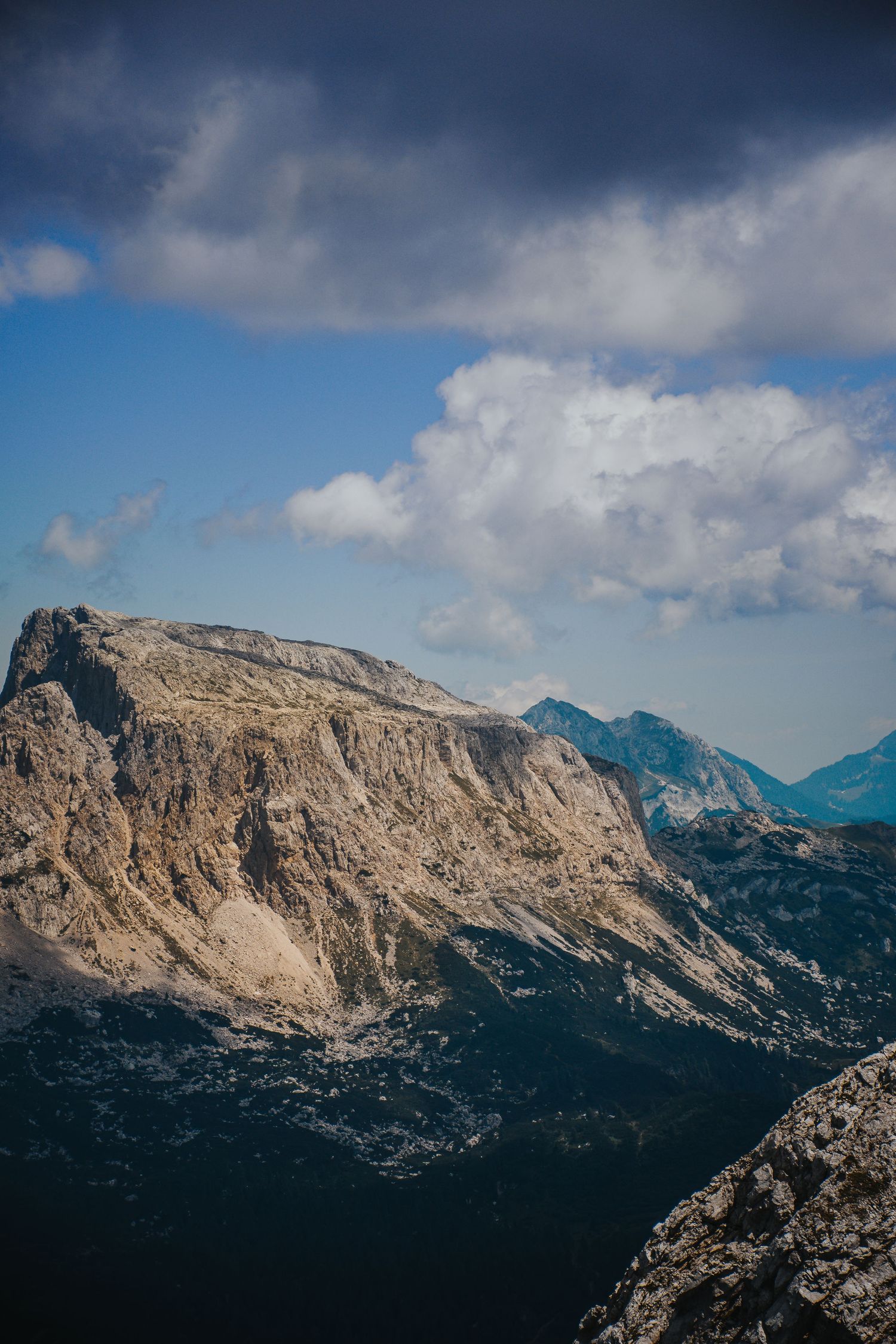 Rugged rocky mountain cliffs rise sharply under a blue sky with white and dark clouds in the Dolomites.