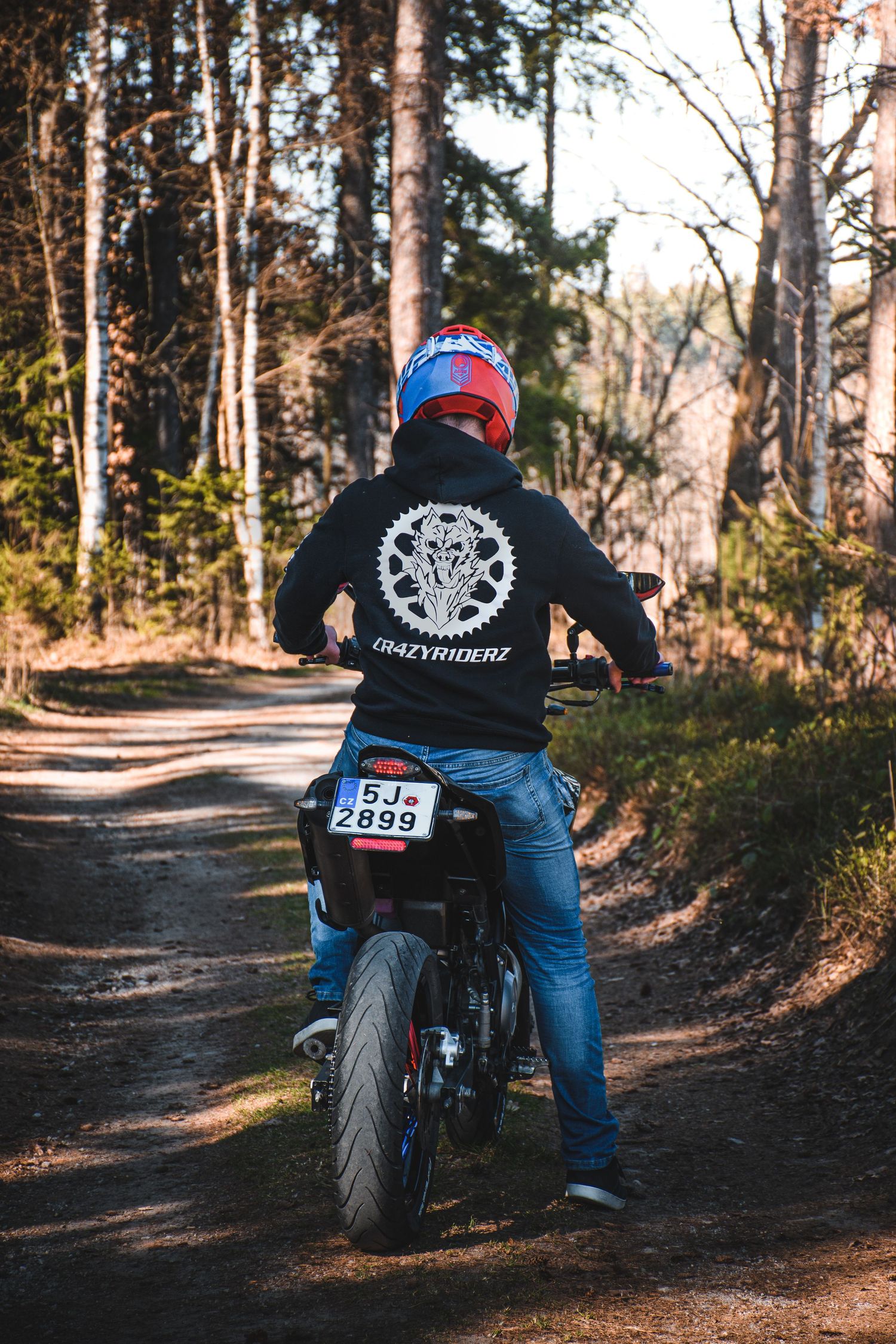 Back view of motorcyclist in GrazyRiderz hoodie riding dirt path in woods.