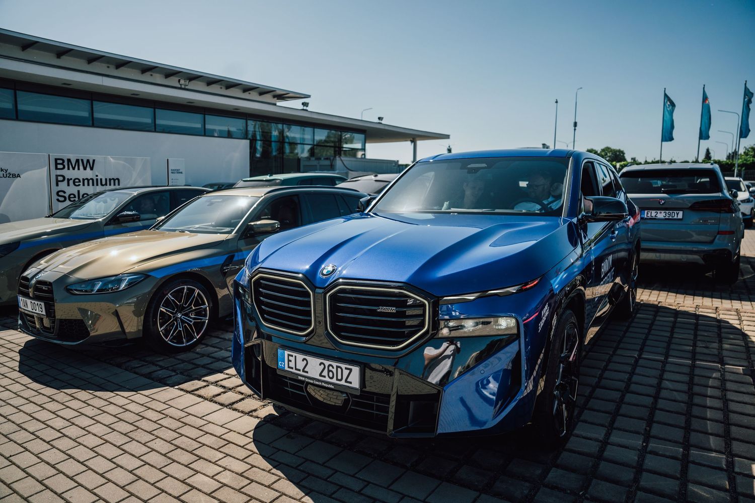 Multiple BMW vehicles including blue XM SUV parked at a BMW Premium dealership on a sunny day.
