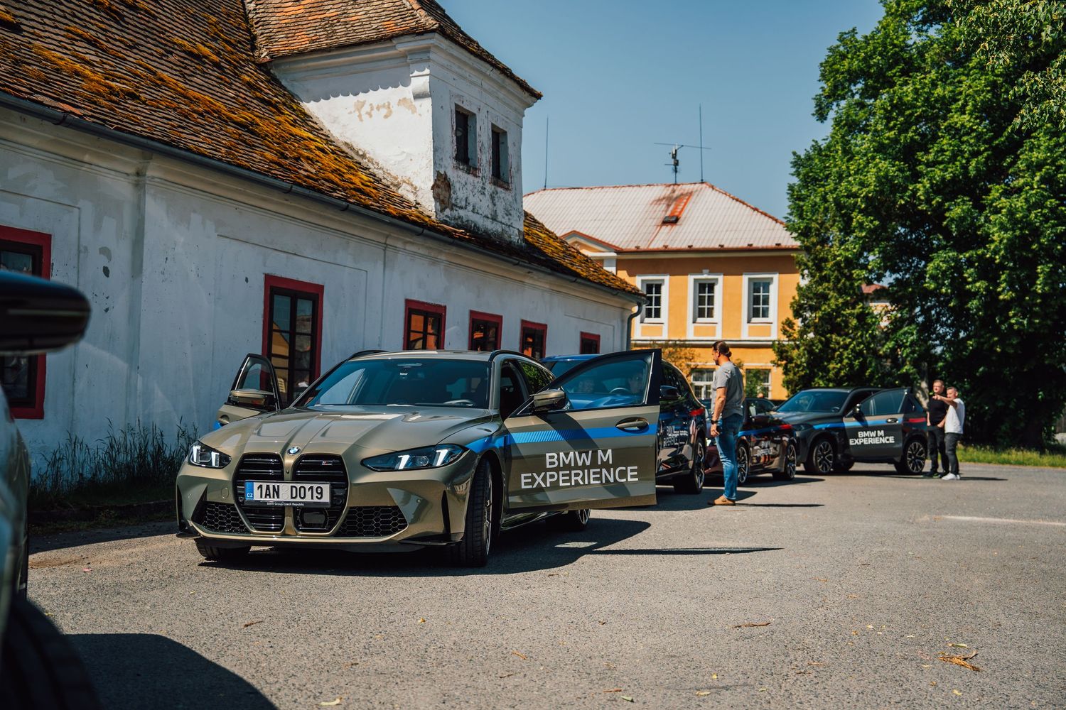 BMW M4 M Experience sedan and other BMW vehicles parked near a historic white European building.