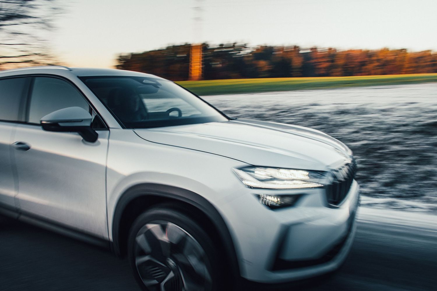 White SUV captured in motion blur speeding along a road at dusk.
