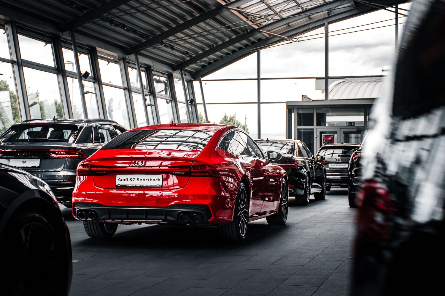 Red Audi S7 Sportback displayed in a modern dealership showroom with other luxury vehicles.