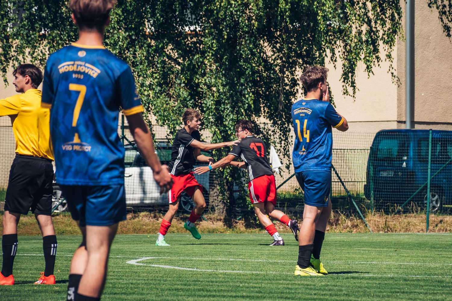 Youth soccer players in black and yellow uniforms compete in a physical outdoor match.