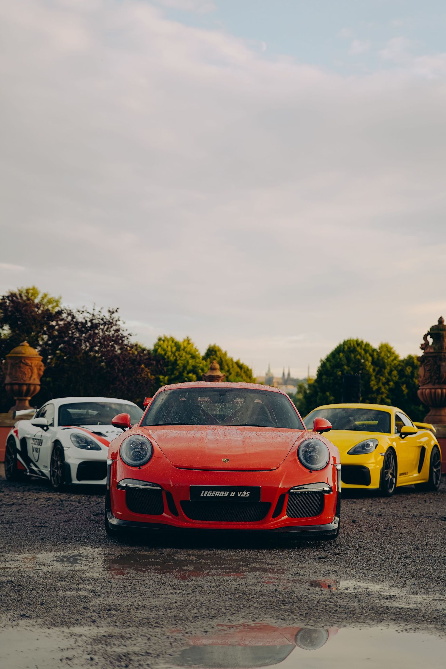 Three Porsche sports cars parked on gravel, red 911 GT3 flanked by white and yellow models.