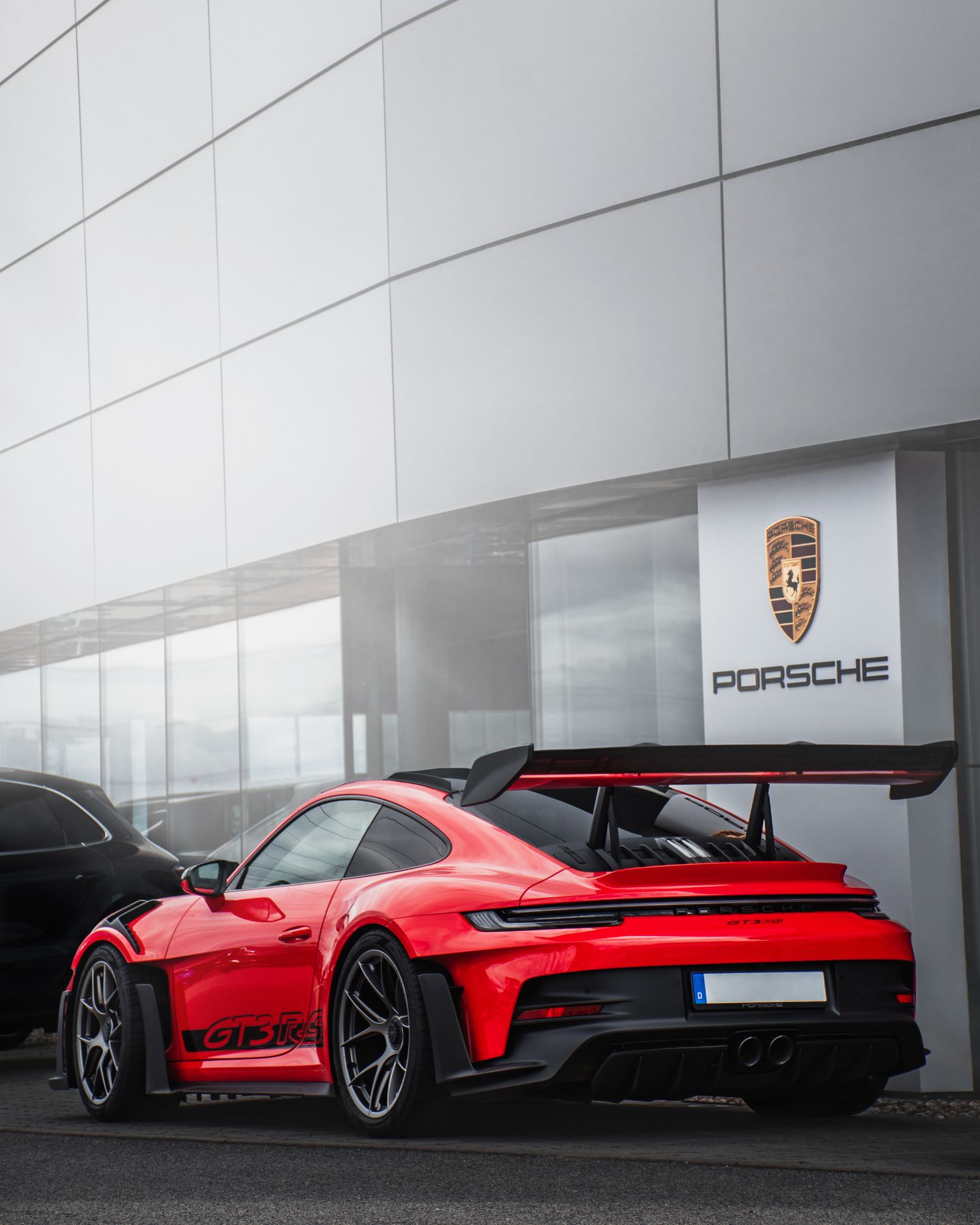 Rear view of a red Porsche 911 GT3 RS with large spoiler outside a Porsche dealership.