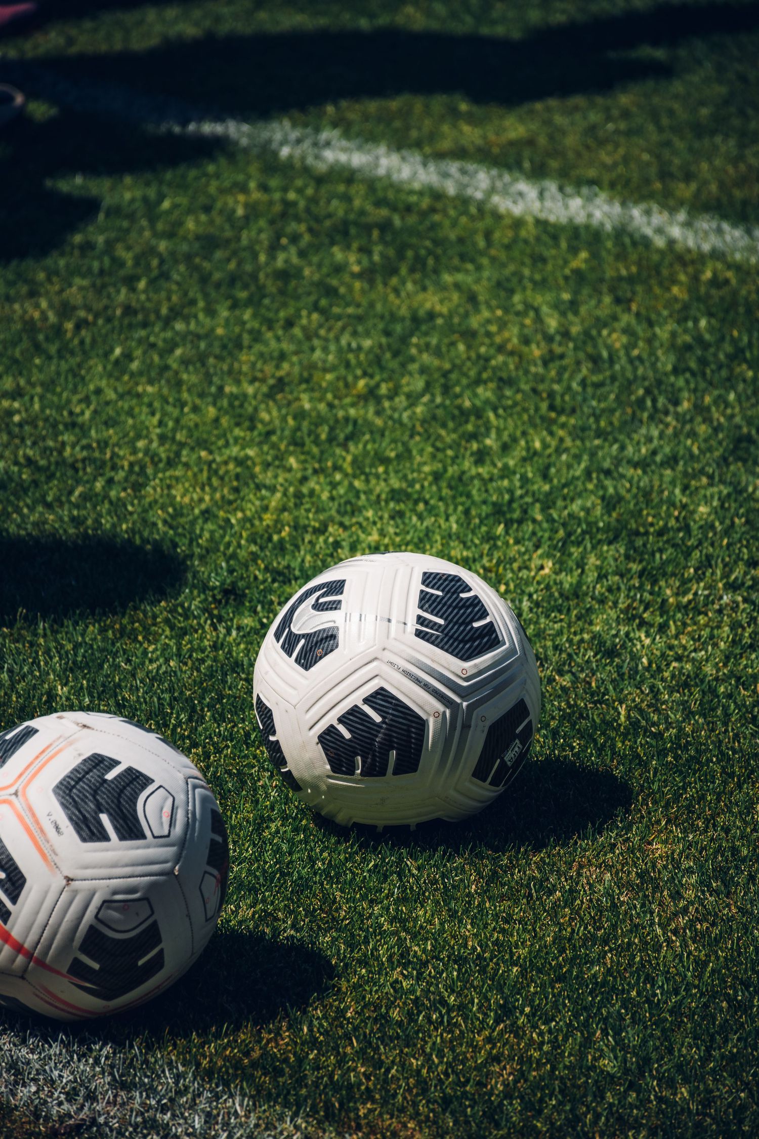 Two white and black Nike soccer balls resting on green grass field near white boundary line.