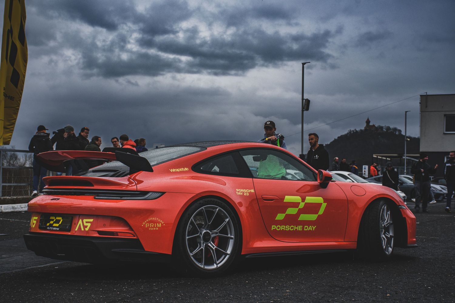 Orange Porsche 911 GT3 with Porsche Day livery at an outdoor motorsport event.