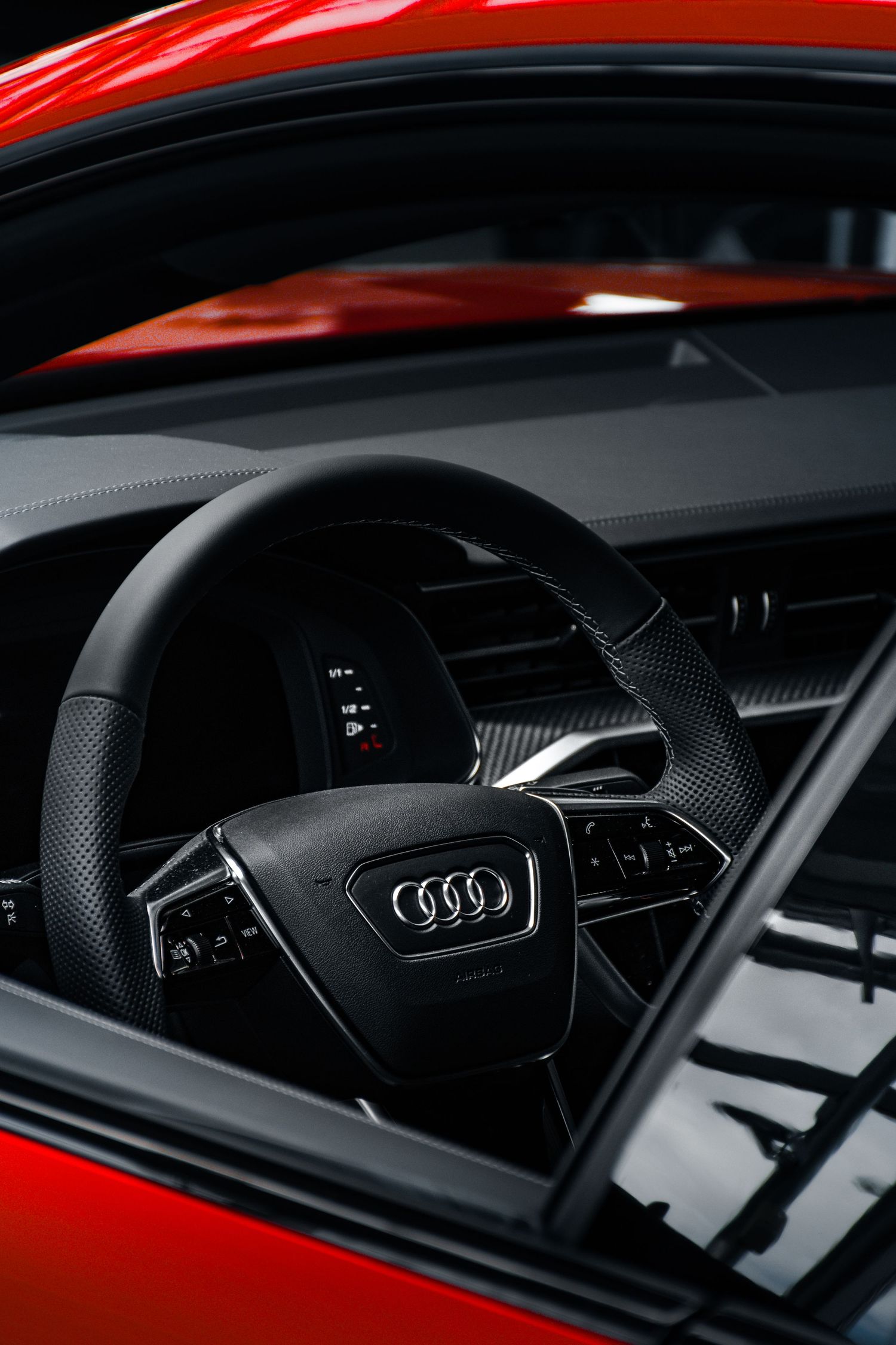 Close-up of Audi four rings logo on black leather steering wheel inside a red Audi vehicle interior.