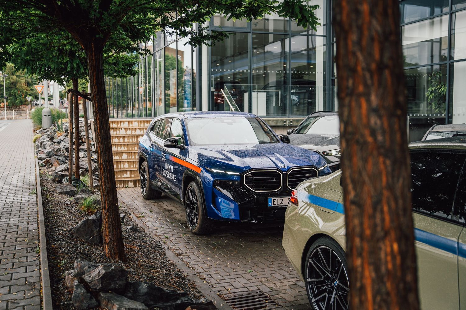 Blue BMW XM with colorful accents parked outside a BMW dealership alongside other luxury vehicles.