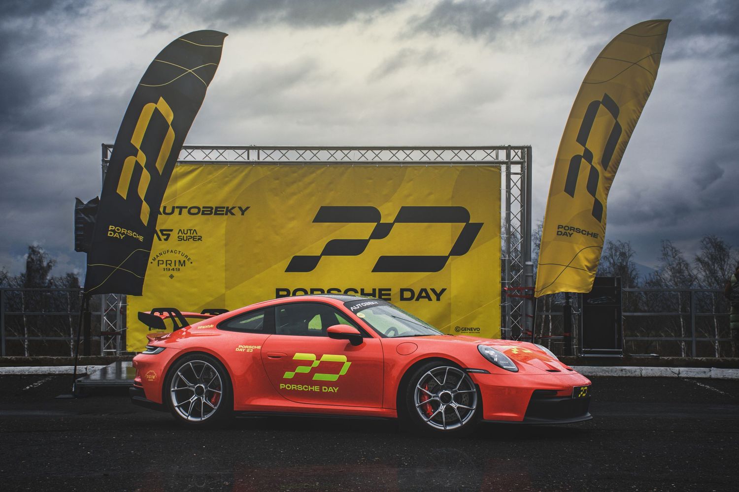 Orange Porsche 911 GT3 displayed at Porsche Day event with yellow branded flags and signage.