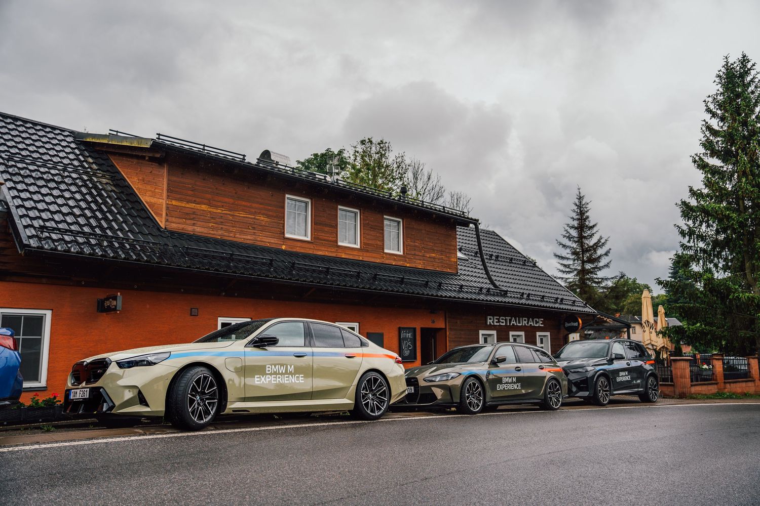 BMW M Experience fleet of cars parked outside a rustic orange building on a rainy day.