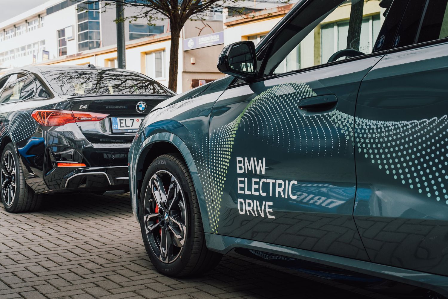 BMW Electric Drive branding on a teal iX SUV parked alongside another BMW vehicle.