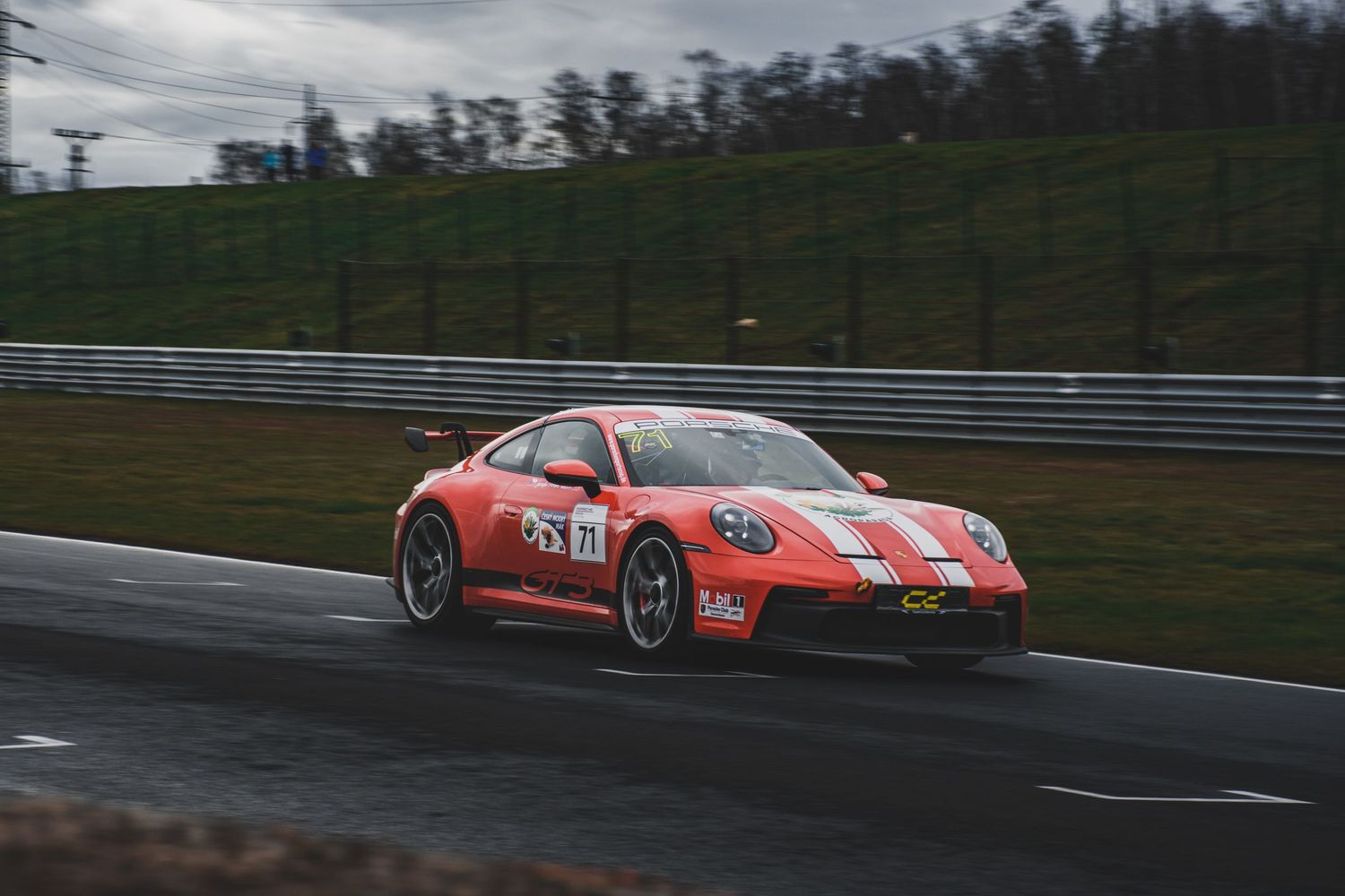 Orange Porsche 911 GT3 Cup race car with white stripes racing on a wet circuit.