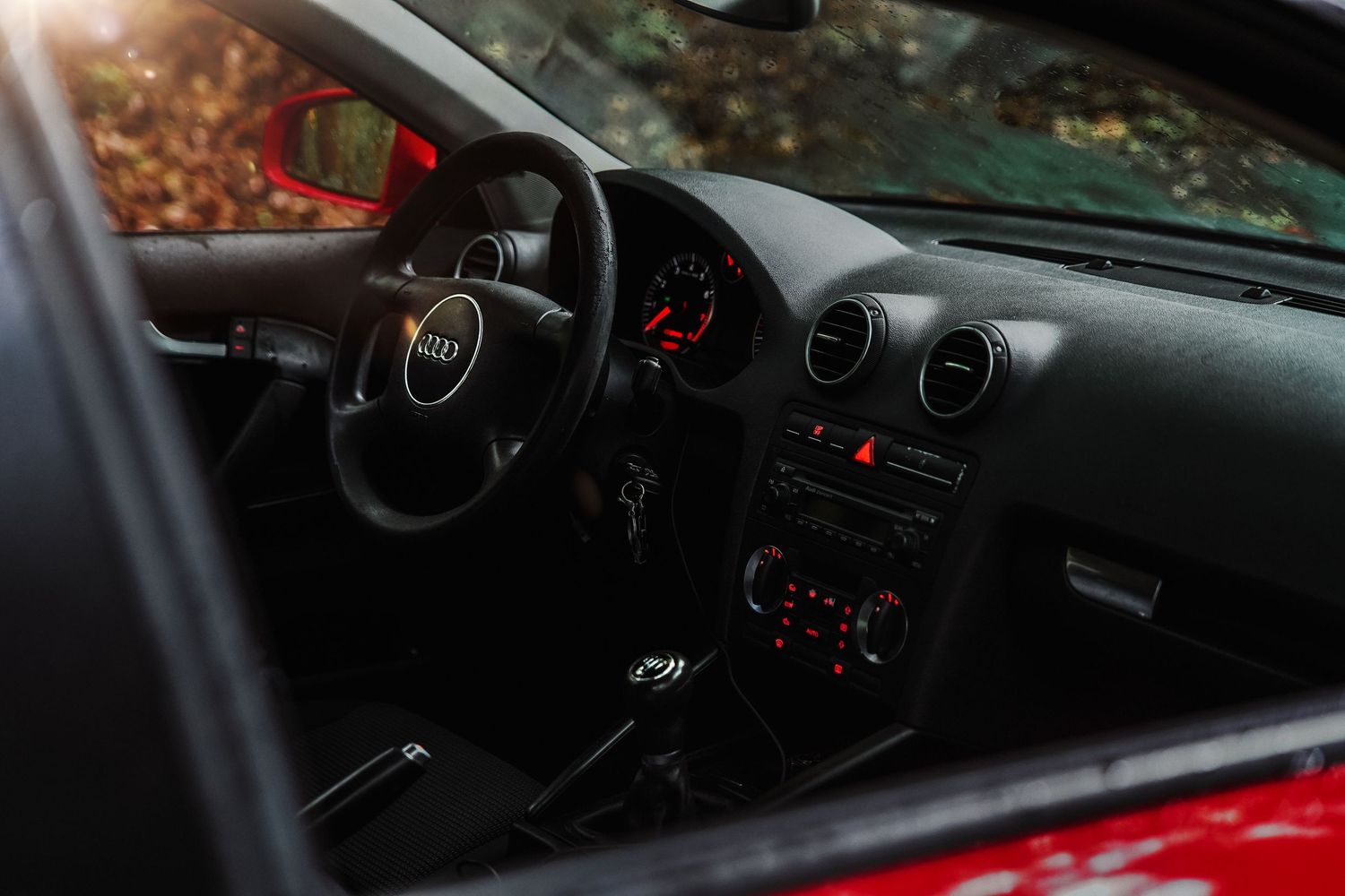 Interior view of red Audi showing steering wheel, dashboard, and center console in autumn setting.