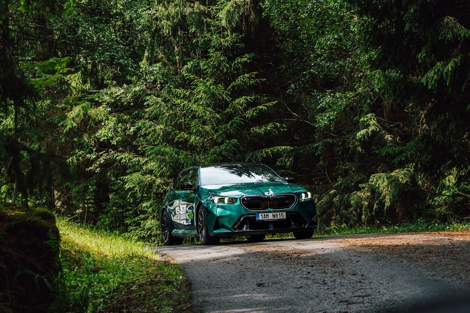 Stunning green BMW M2 parked on a forest road surrounded by lush evergreen trees.