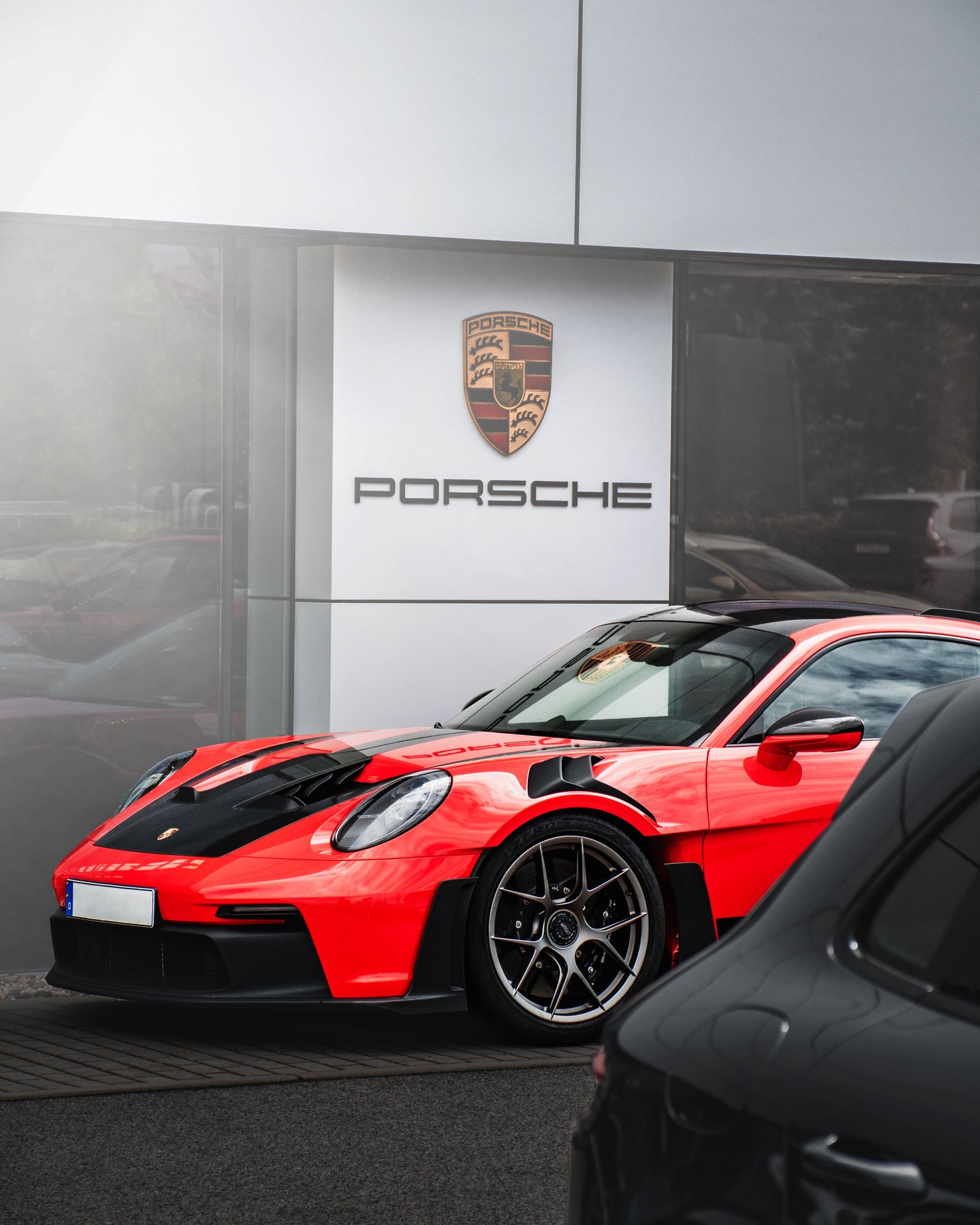 Red Porsche 911 GT3 RS parked in front of an official Porsche dealership on a cloudy day.