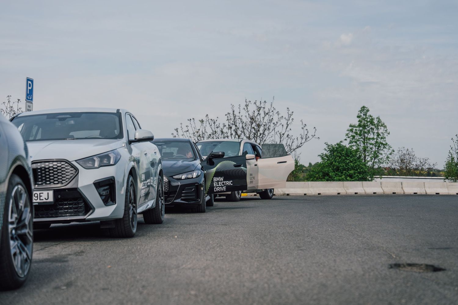Row of luxury SUVs including a white crossover parked in an open lot under a partly cloudy sky.