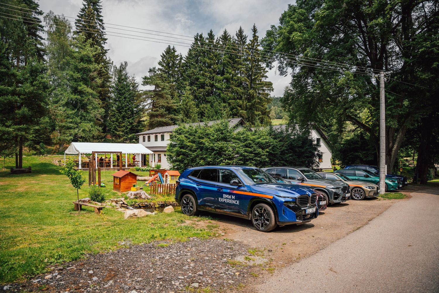 Blue BMW SUV and other cars parked outside a forest retreat surrounded by tall green trees.