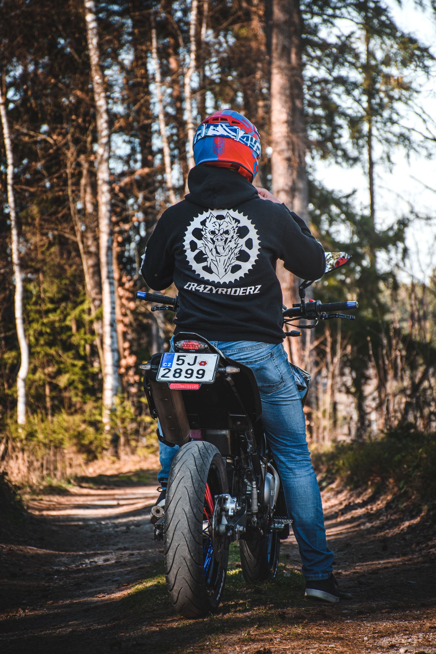 Rear view of GrazyRiderz hoodie biker on motorcycle on forest path.