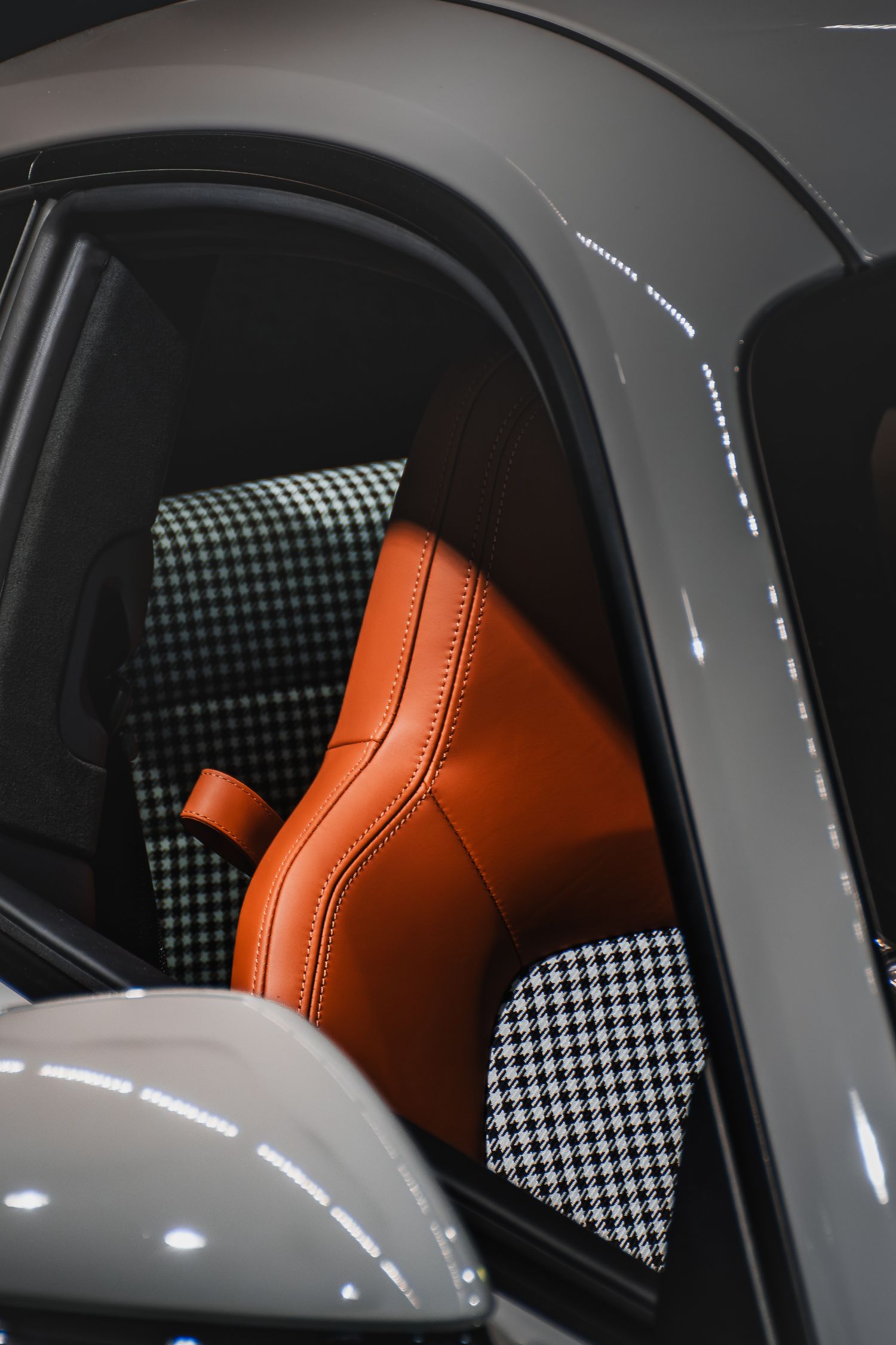 Luxury car interior featuring orange leather bucket seat with black houndstooth pattern upholstery.
